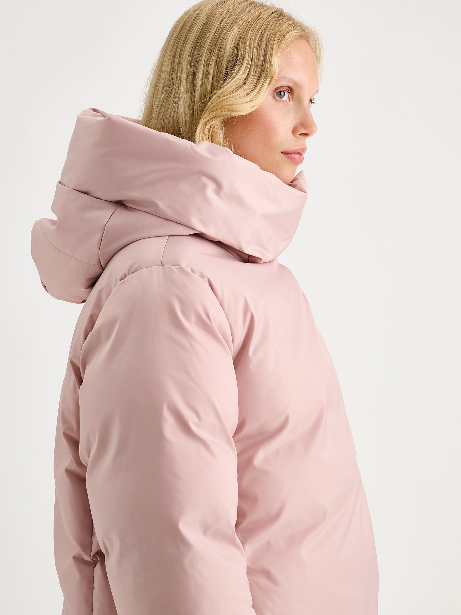 Warm and wonderfully voluminous, the long Inari puffer coat in light pink, on a model.