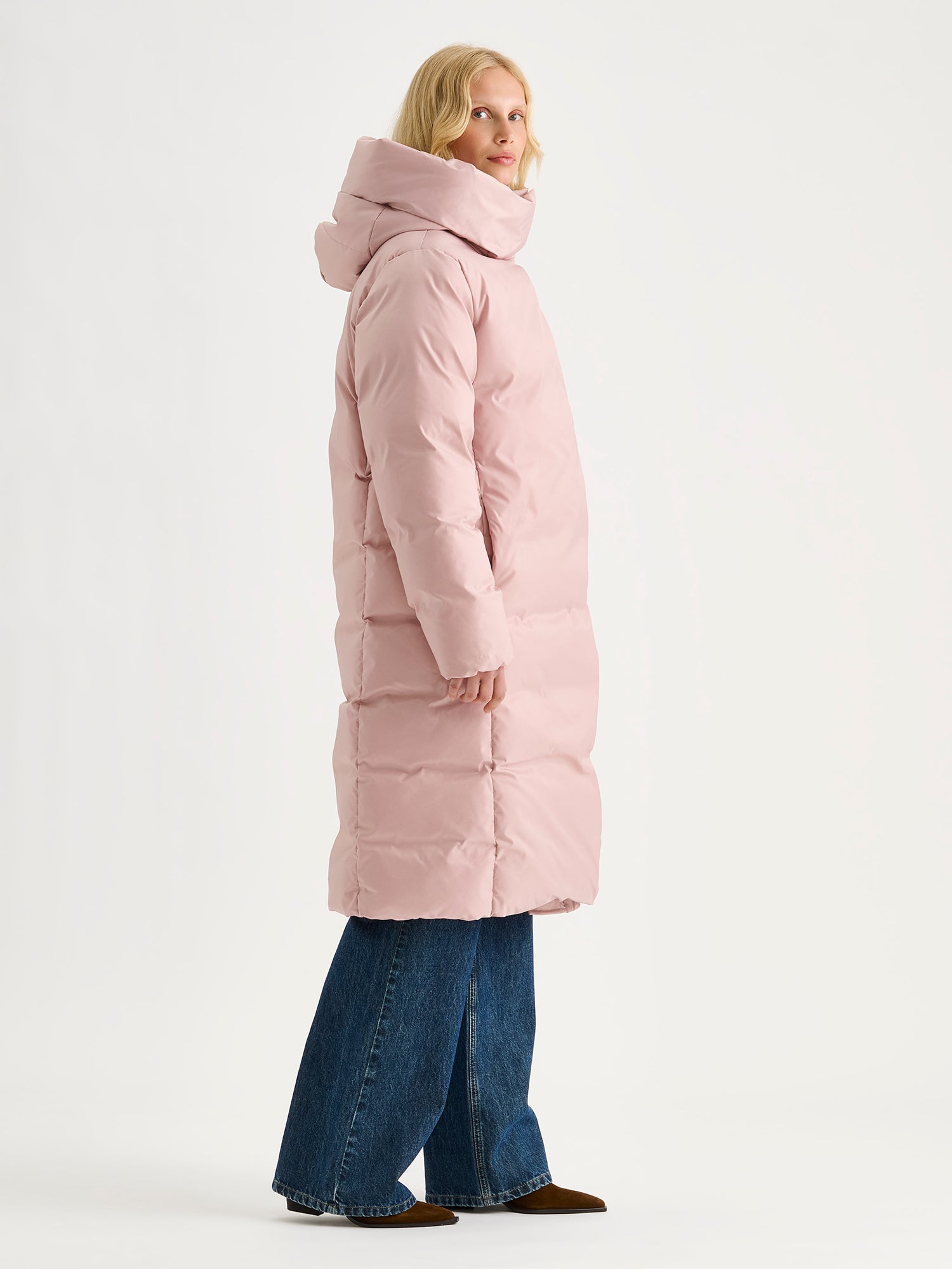 Warm and wonderfully voluminous, the long Inari puffer coat in light pink, on a model. Side view