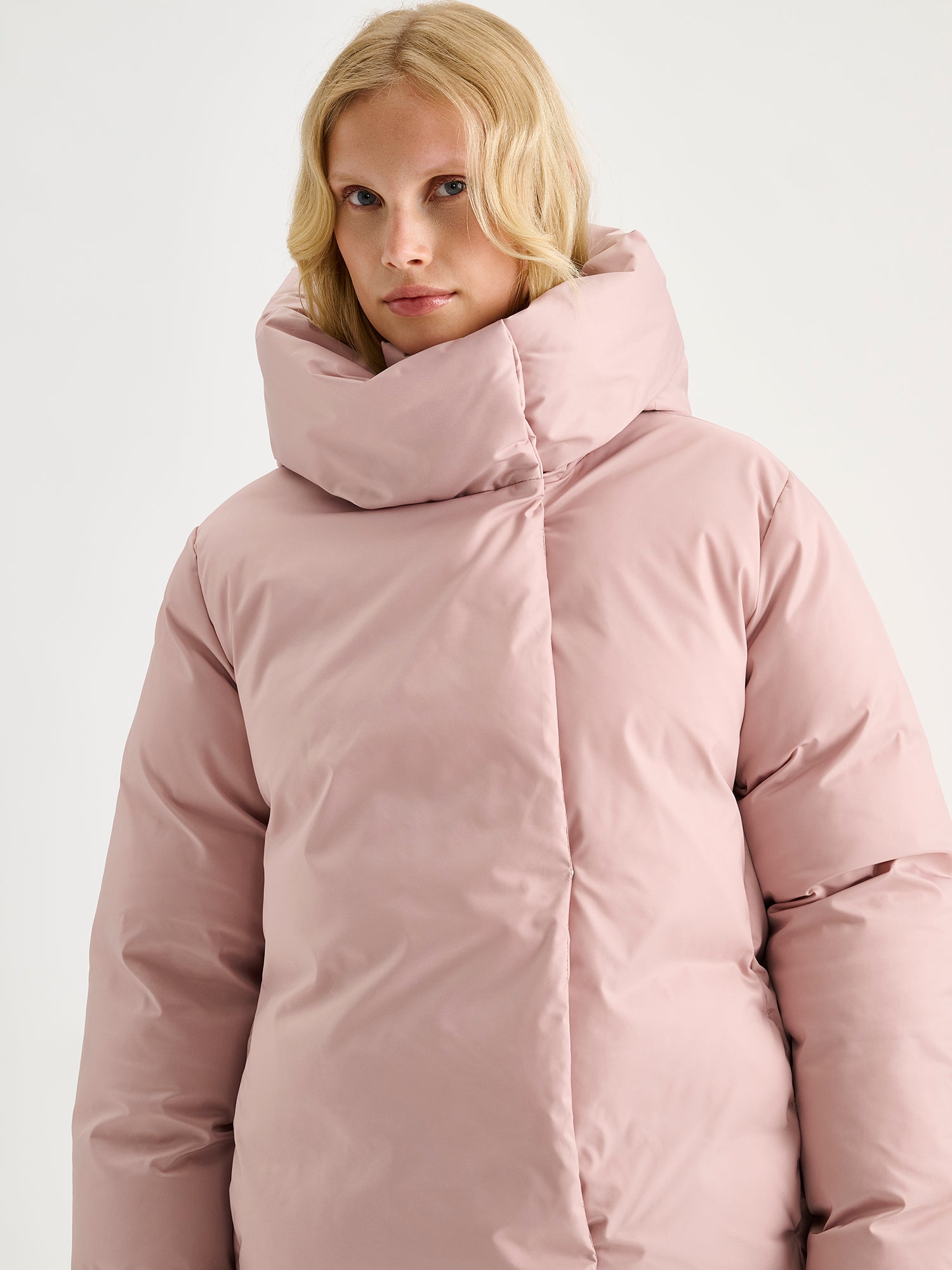Warm and wonderfully voluminous, the long Inari puffer coat in light pink, on a model close-up.