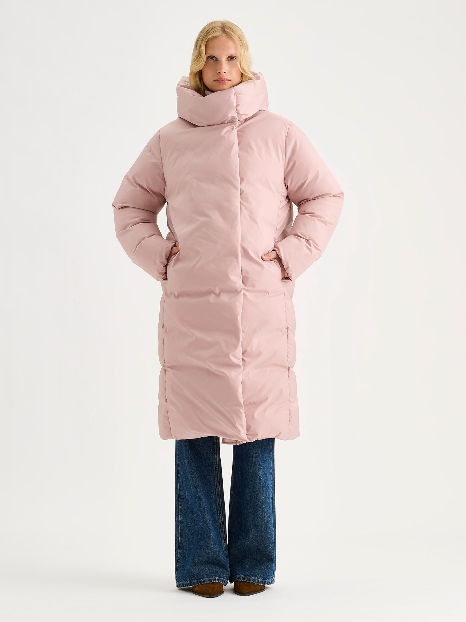 Warm and wonderfully voluminous, the long Inari puffer coat in light pink, on a model.