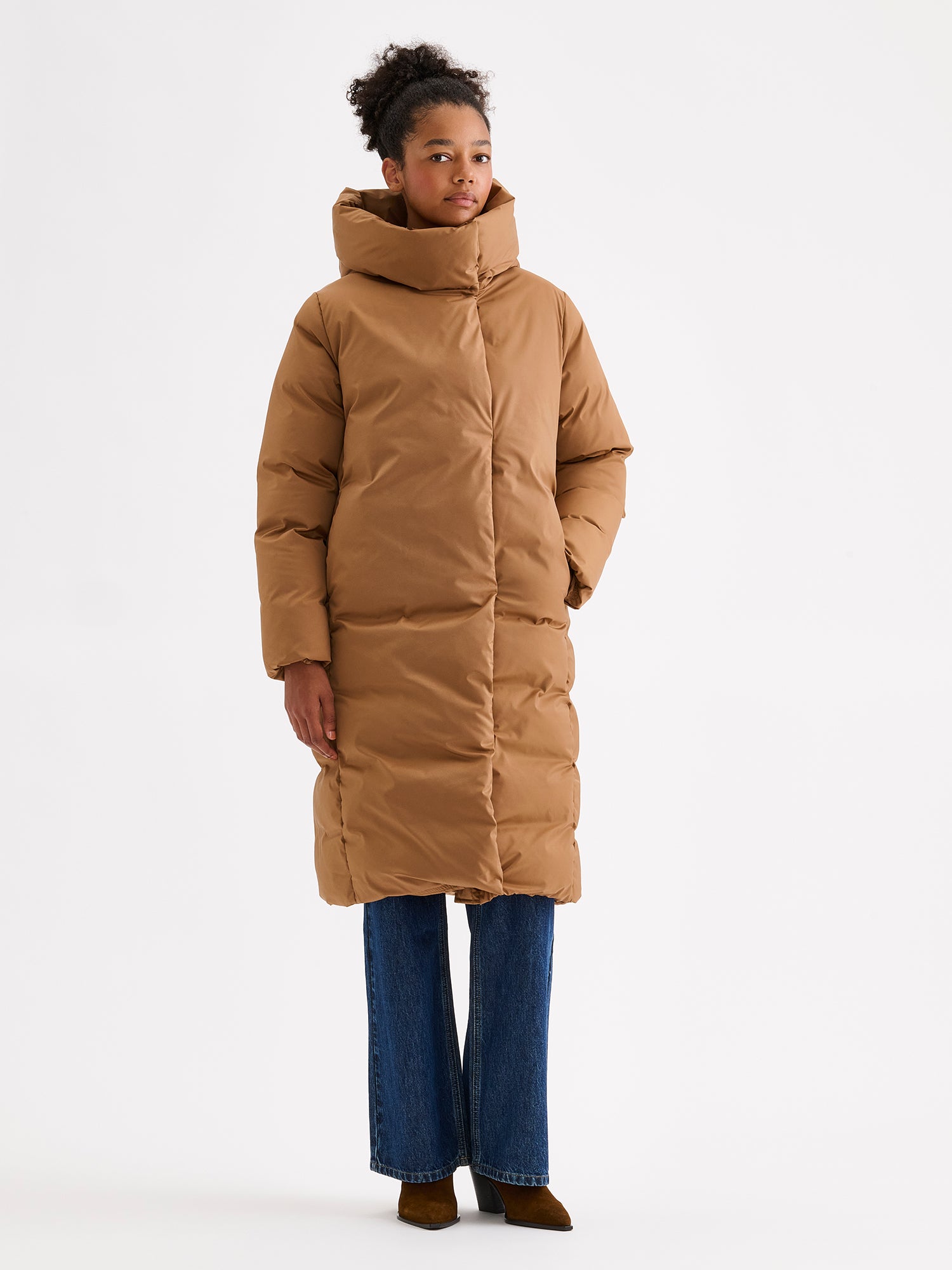 Warm and wonderfully voluminous, the long Inari puffer coat in brown. On a model with jeans