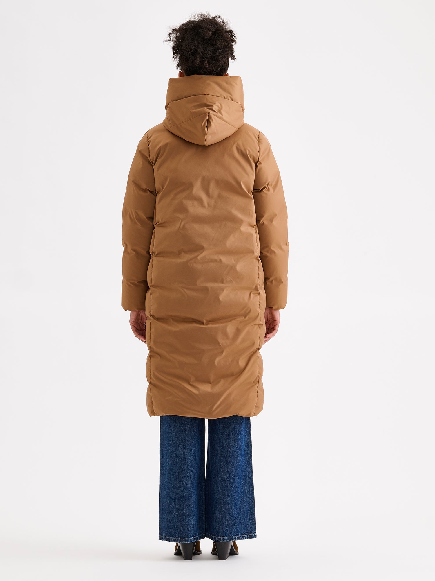 Warm and wonderfully voluminous, the long Inari puffer coat in brown. On a model with jeans, from the backside.