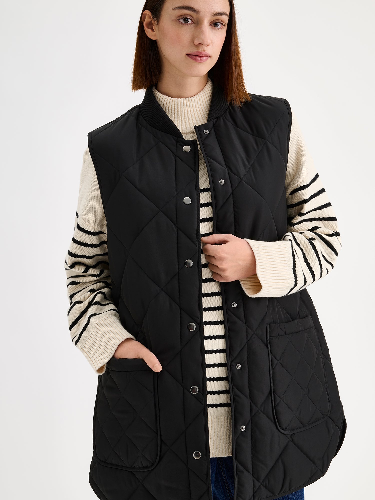 Nanso women's beautiful classic quilted vest in black, on a model with a striped sweater and wide blue jeans.