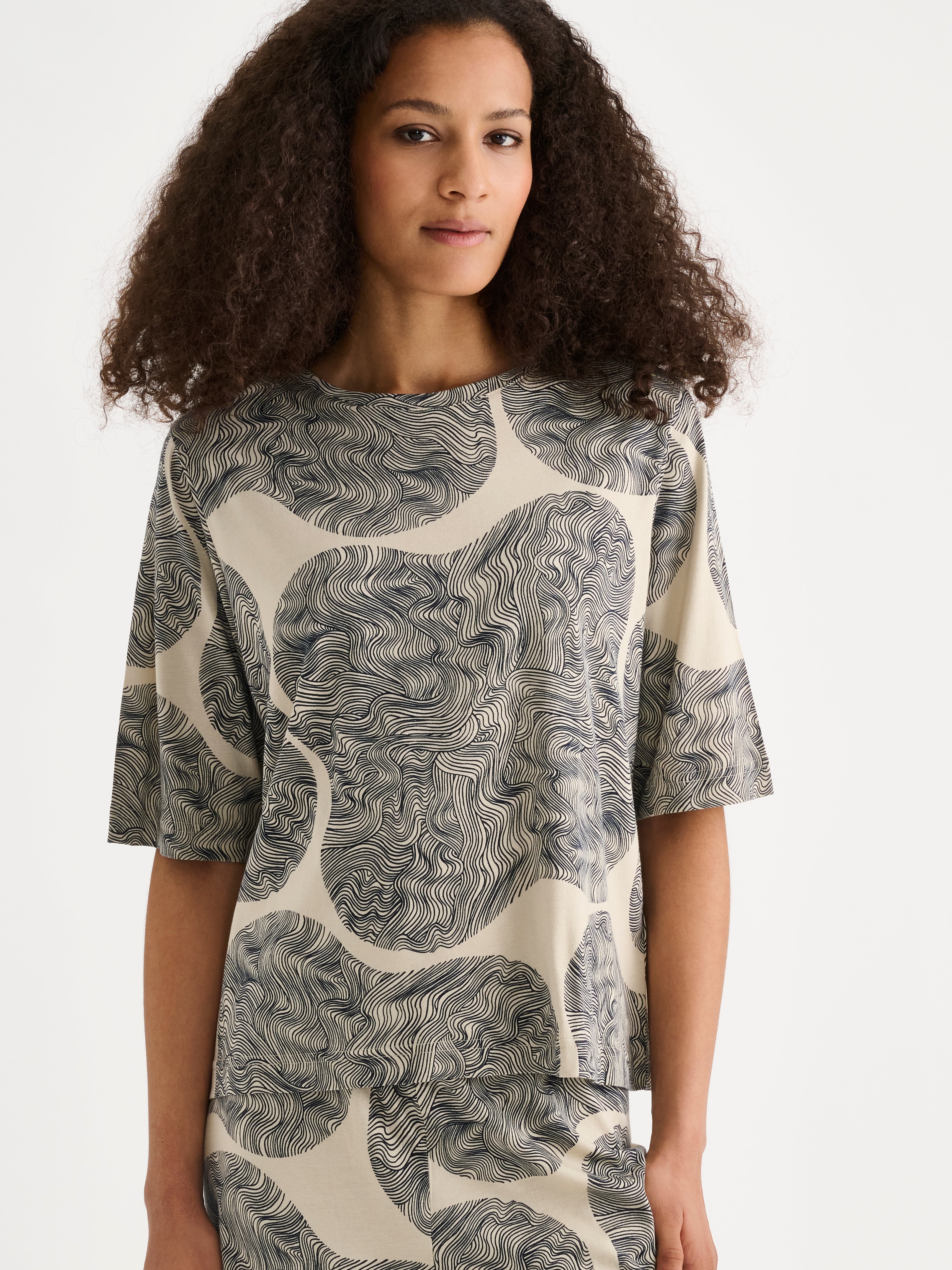 The straight-cut Paasi T-shirt for women, featuring a harmonious all-over print, is perfect for relaxed moments at home, on a model close-up.