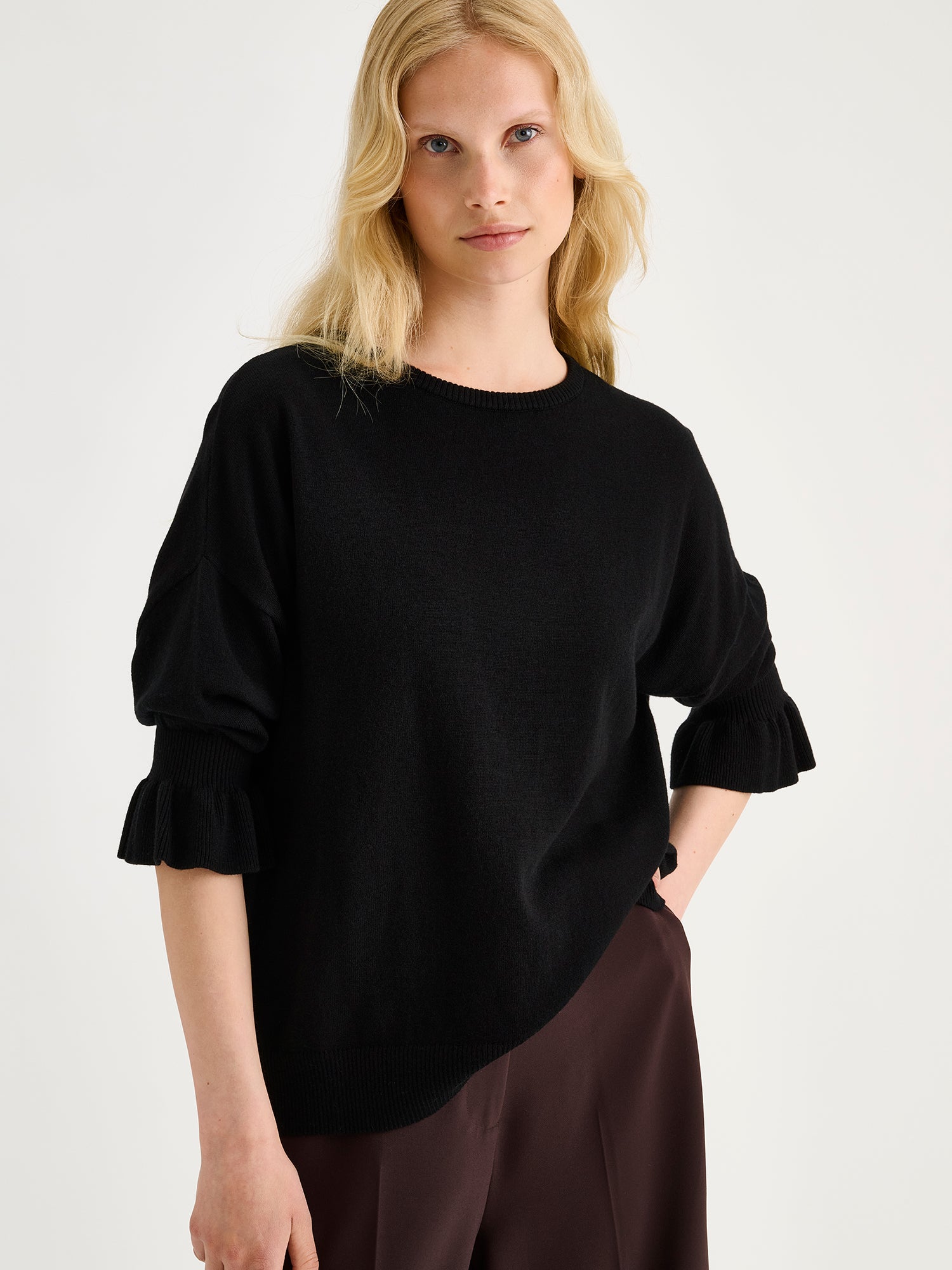 Nanso women's simply stylish and lightweight Villis Frilla knit jumper is charmingly finished with beautiful frill details at the cuffs, on a model with brown trousers