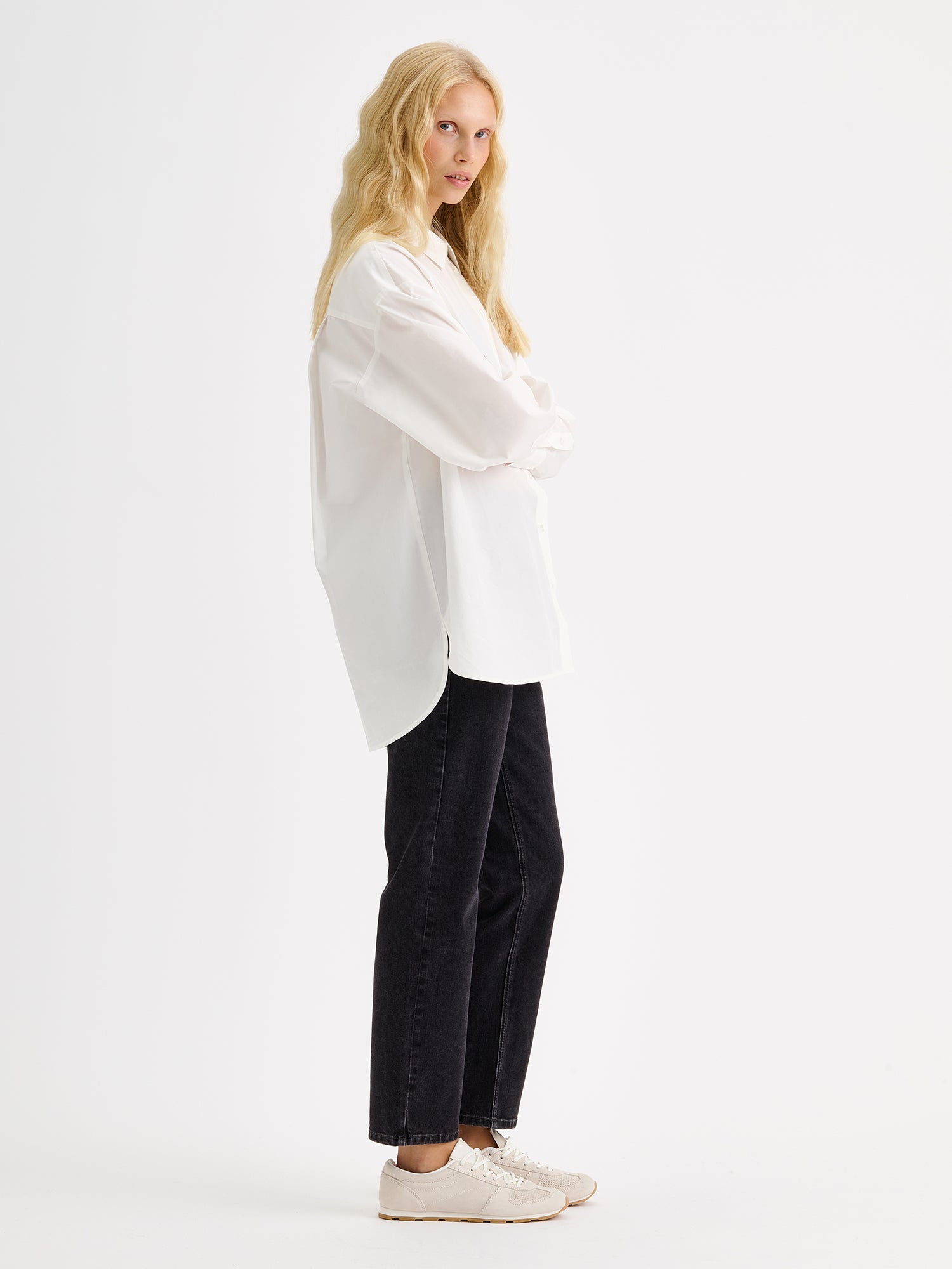 Nanso womens relaxed-fit white Sofi shirt pictured on a model with black jeans, from the side angle.