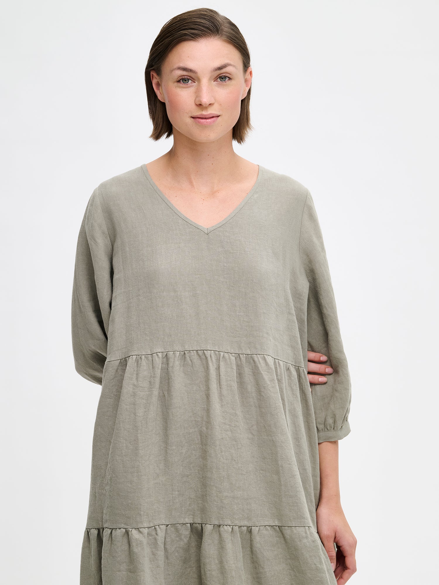 Nanso women's SARALIVIA linen dress in green features charming layered ruffles, 3/4 sleeves, side pockets and a V-neckline. Pictured on a model, close-up.