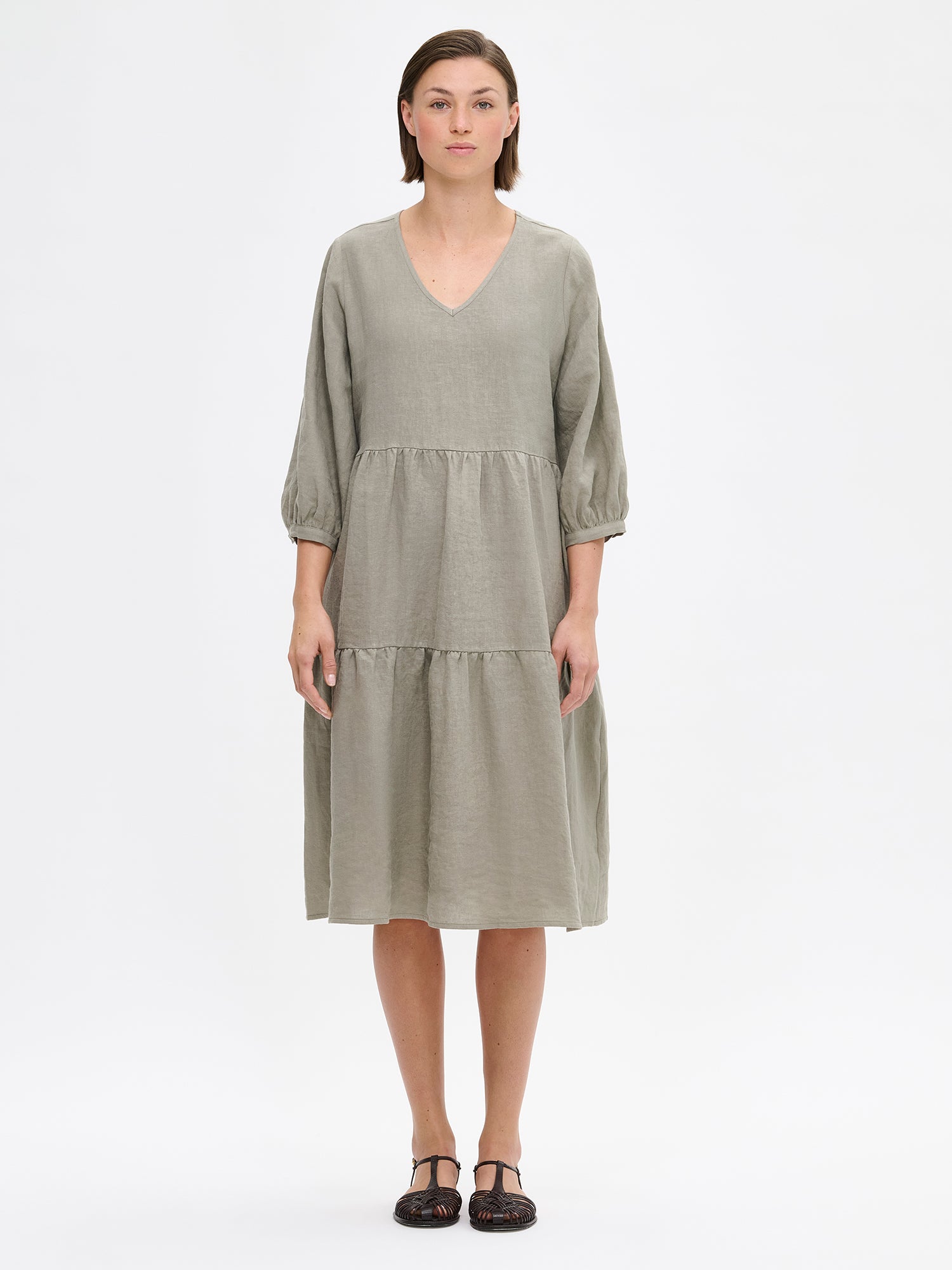 Nanso women's SARALIVIA linen dress in green features charming layered ruffles, 3/4 sleeves, side pockets and a V-neckline. Pictured on a model with sandals on.