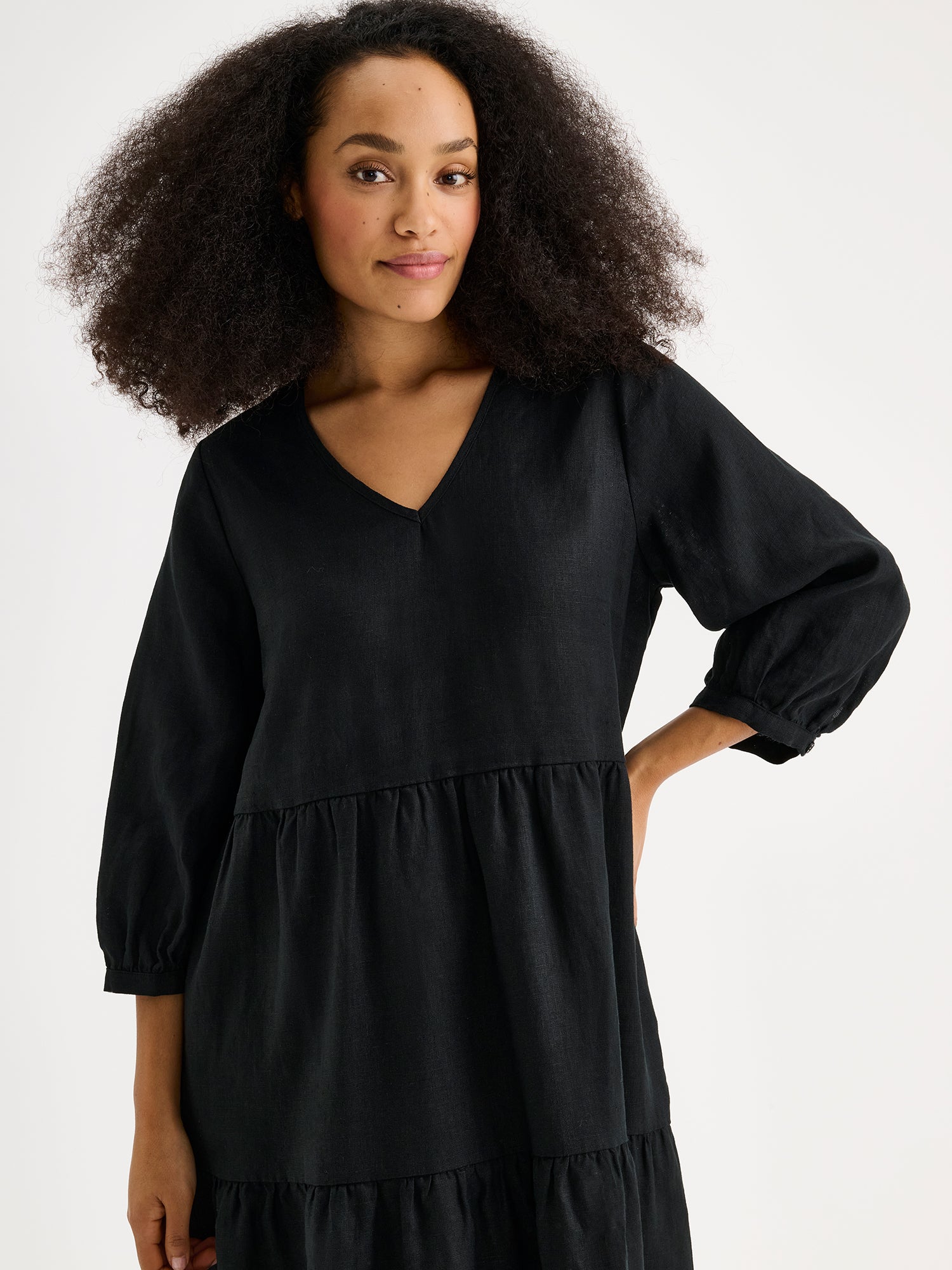Nanso women's SARALIVIA linen dress in black features charming layered ruffles, 3/4 sleeves, side pockets and a V-neckline. Pictured on a model, close-up.