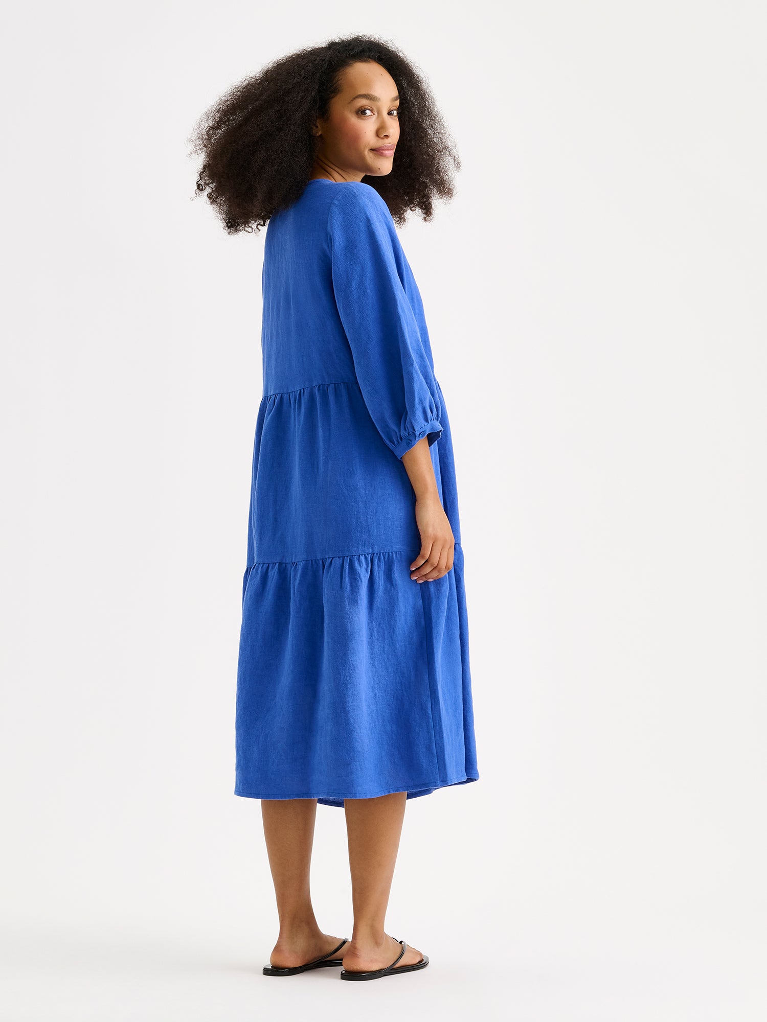 Nanso women's SARALIVIA linen dress in blue features charming layered ruffles, 3/4 sleeves, side pockets and a V-neckline. On a model from the backside.