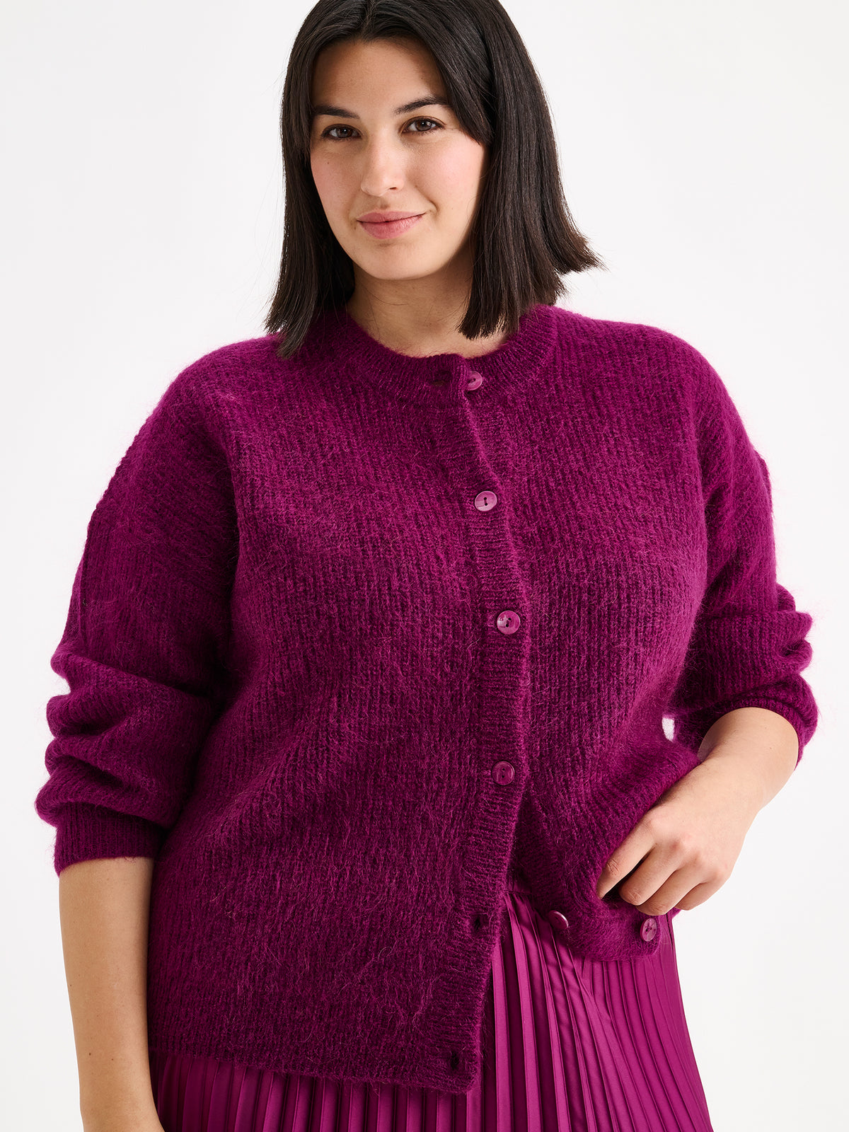 Nanso women's wonderfully warm and luxurious Sumi cardigan enchants with its vibrant violet hue and beautifully fluffy texture, pictured on a model with a pleated skirt.