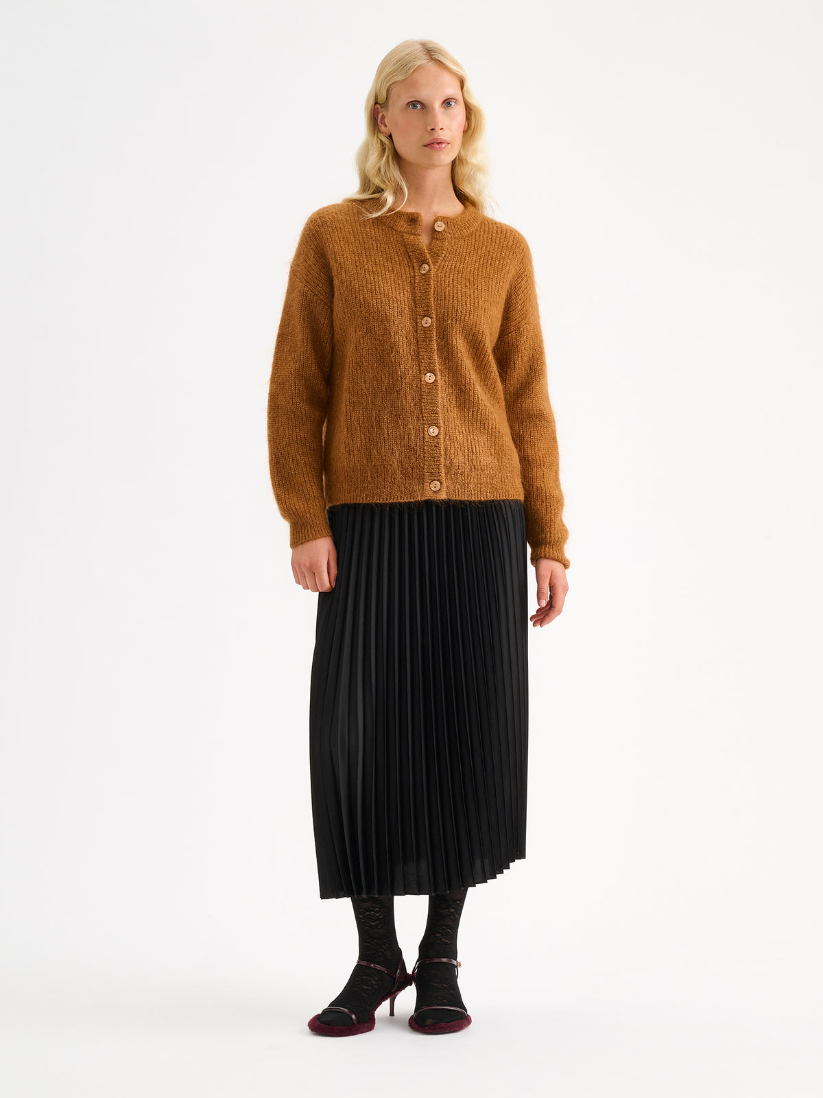 Nanso women's wonderfully warm and luxurious Sumi cardigan enchants with its rich brown hue and beautifully fluffy texture. On a model with  black skirt and heels.