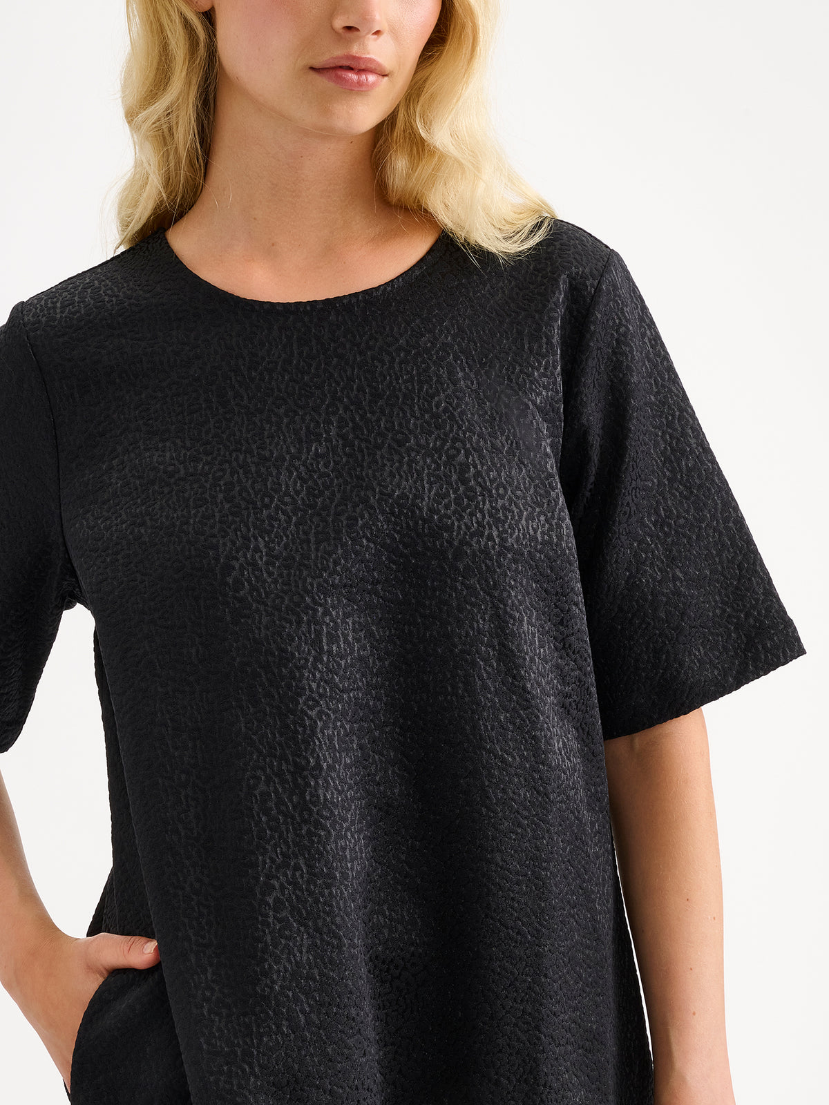 Nanso women's striking black Leora dress captivates with its beautiful fabric, combining a festive sheen with a rich textured surface, on a model close-up.