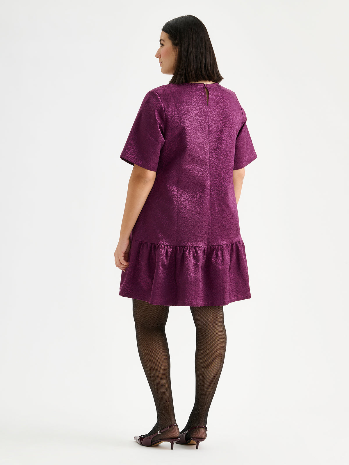 Nanso women's striking Leora dress captivates with its beautiful fabric, combining a festive sheen with a rich textured surface, pictured on a model with heels, from the backside.