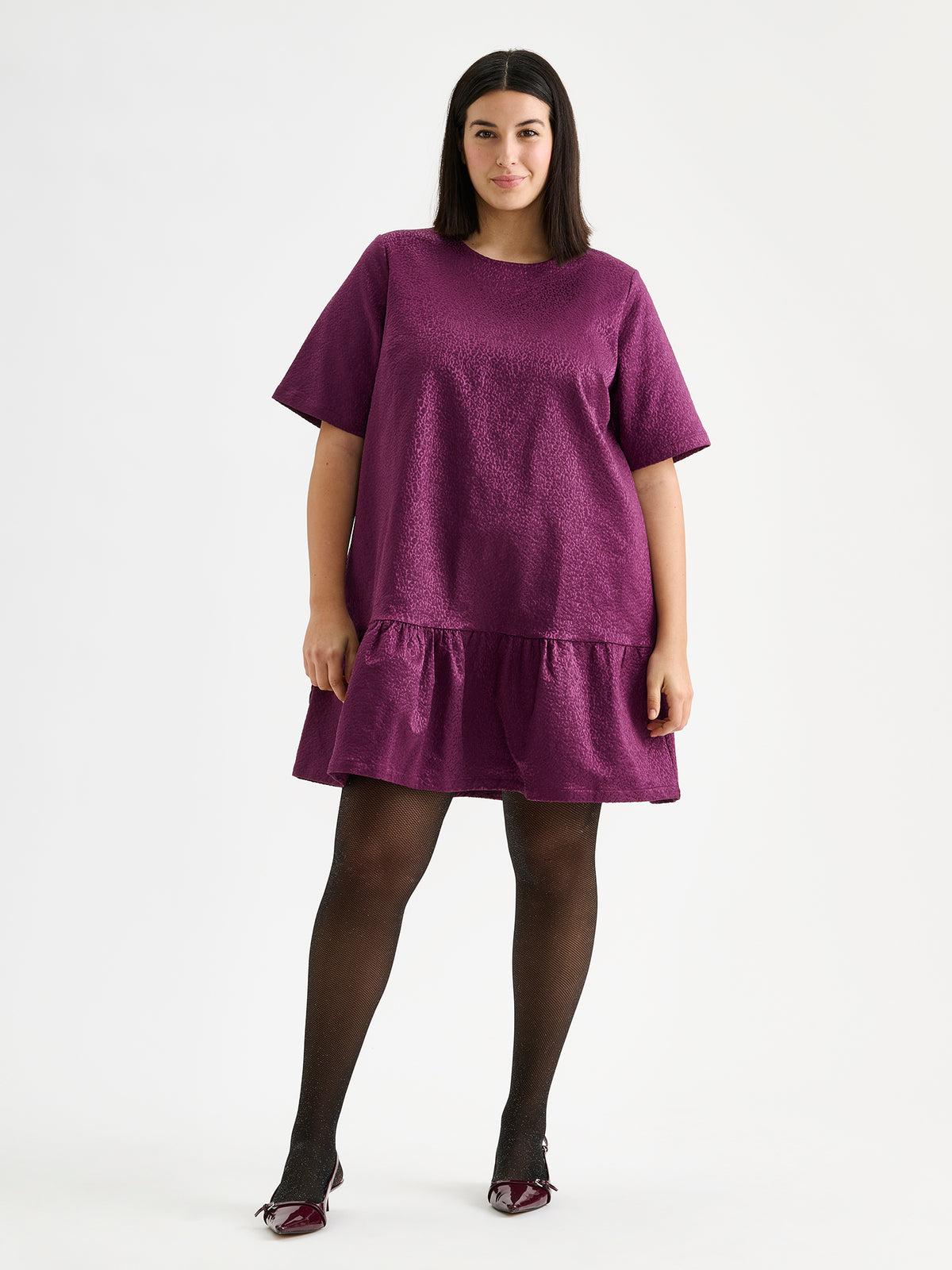 Nanso women's striking Leora dress captivates with its beautiful fabric, combining a festive sheen with a rich textured surface, pictured on a model with heels.
