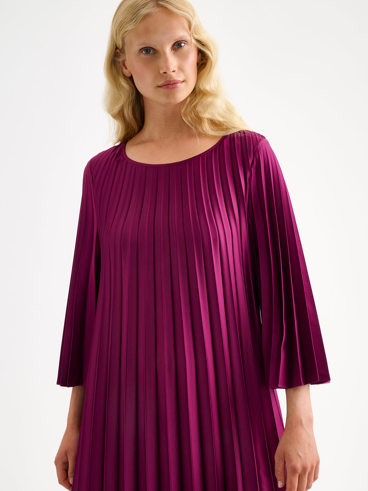 Nanso women's beautifully draping Taite dress in a deliciously radiant violet shade. This versatile pleated dress can be worn with or without the slim belt. This A-line dress features 3/4-length sleeves and a slim belt at the waist. Pictured on a model close-up.