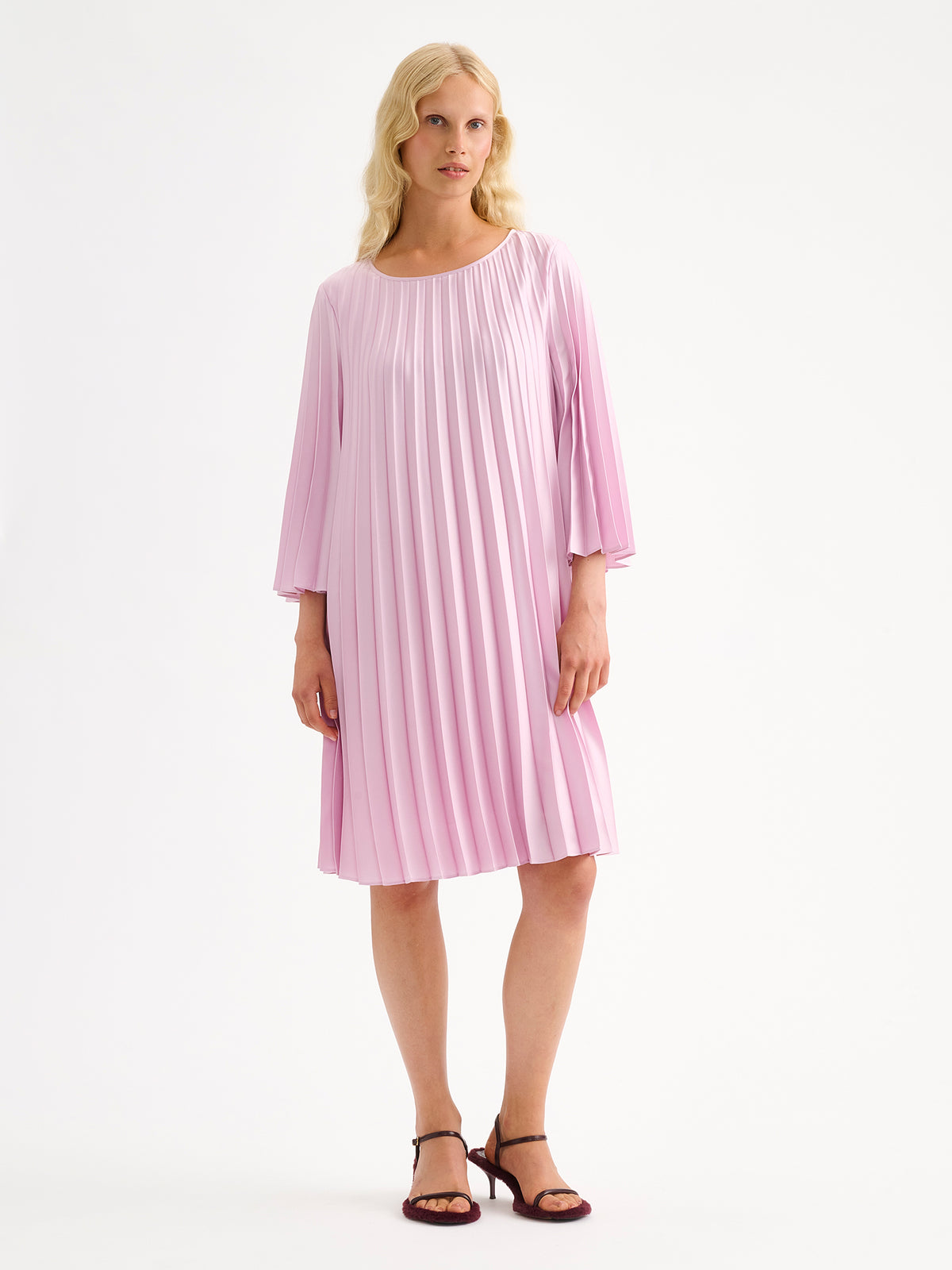 Nanso women's beautifully draping Taite dress in a deliciously cool light pink shade. This versatile pleated dress can be worn with or without the slim belt. This A-line dress features 3/4-length sleeves and a slim belt at the waist. Pictured on a model with heels.