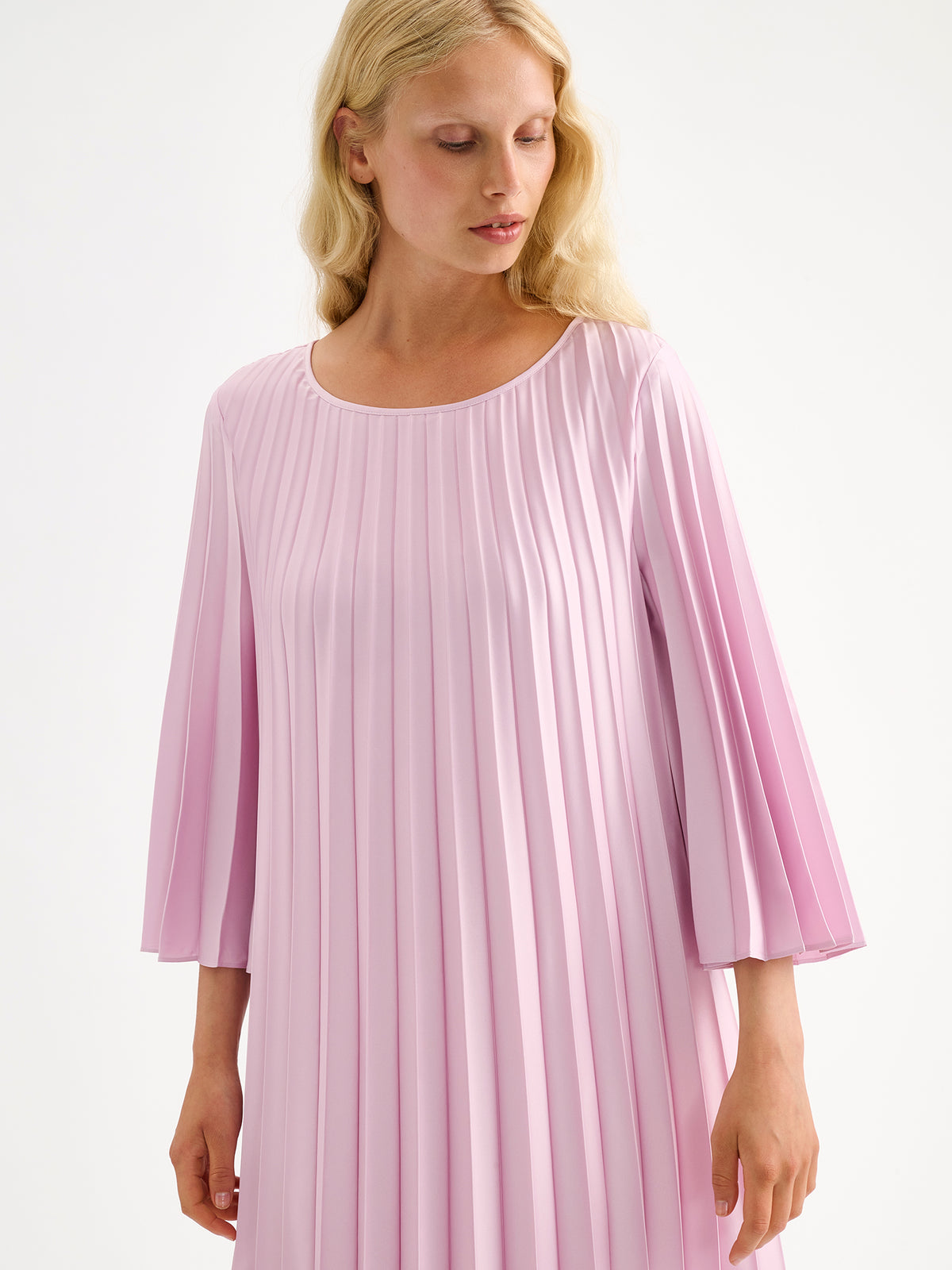 Nanso women's beautifully draping Taite dress in a deliciously cool light pink shade. This versatile pleated dress can be worn with or without the slim belt. This A-line dress features 3/4-length sleeves and a slim belt at the waist. Pictured on a model close-up.