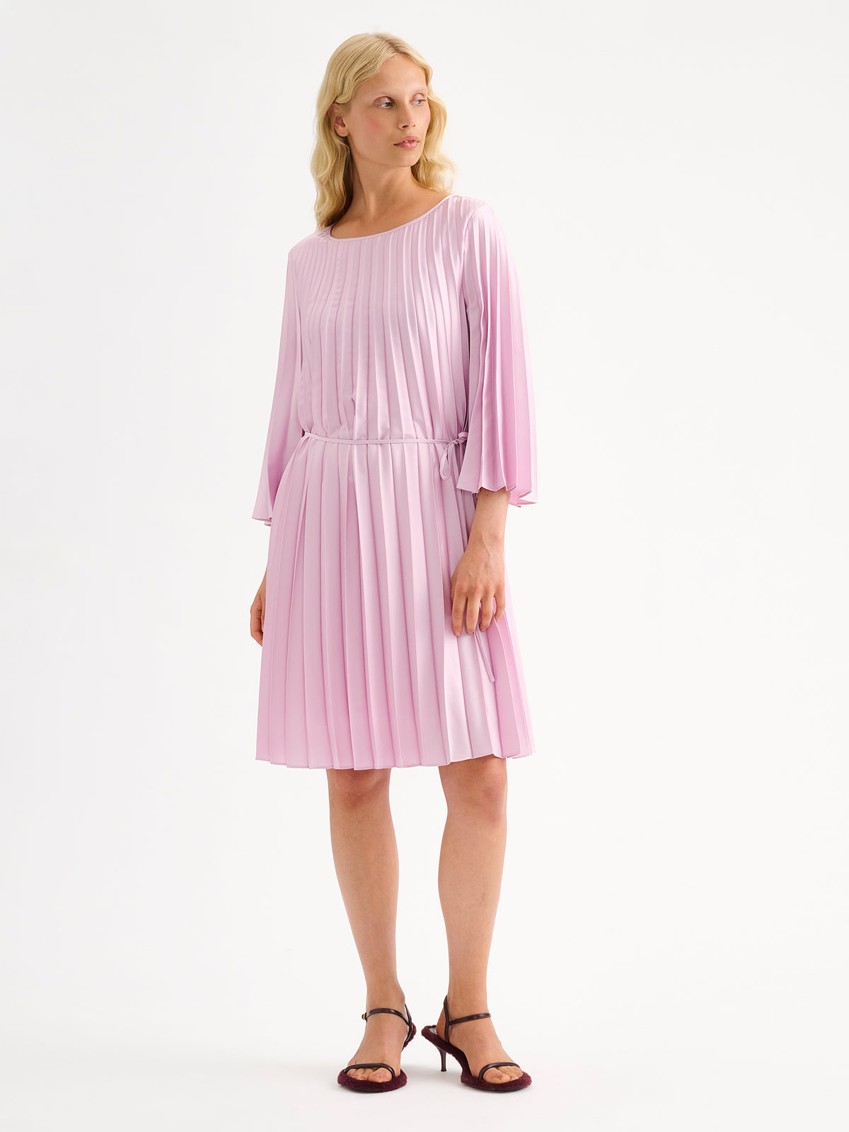 Nanso women's beautifully draping Taite dress in a deliciously cool light pink shade. This versatile pleated dress can be worn with or without the slim belt. This A-line dress features 3/4-length sleeves and a slim belt at the waist. Pictured on a model with heels.
