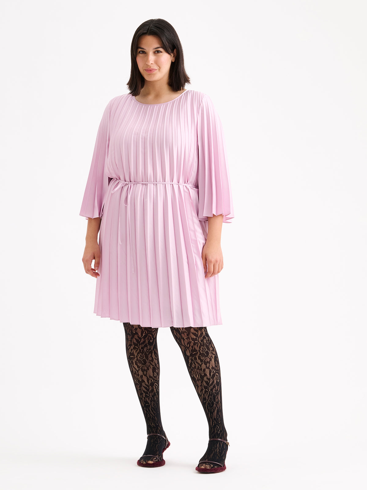 Nanso women's beautifully draping Taite dress in a deliciously cool light pink shade. This versatile pleated dress can be worn with or without the slim belt. This A-line dress features 3/4-length sleeves and a slim belt at the waist. Pictured on a model with heels.