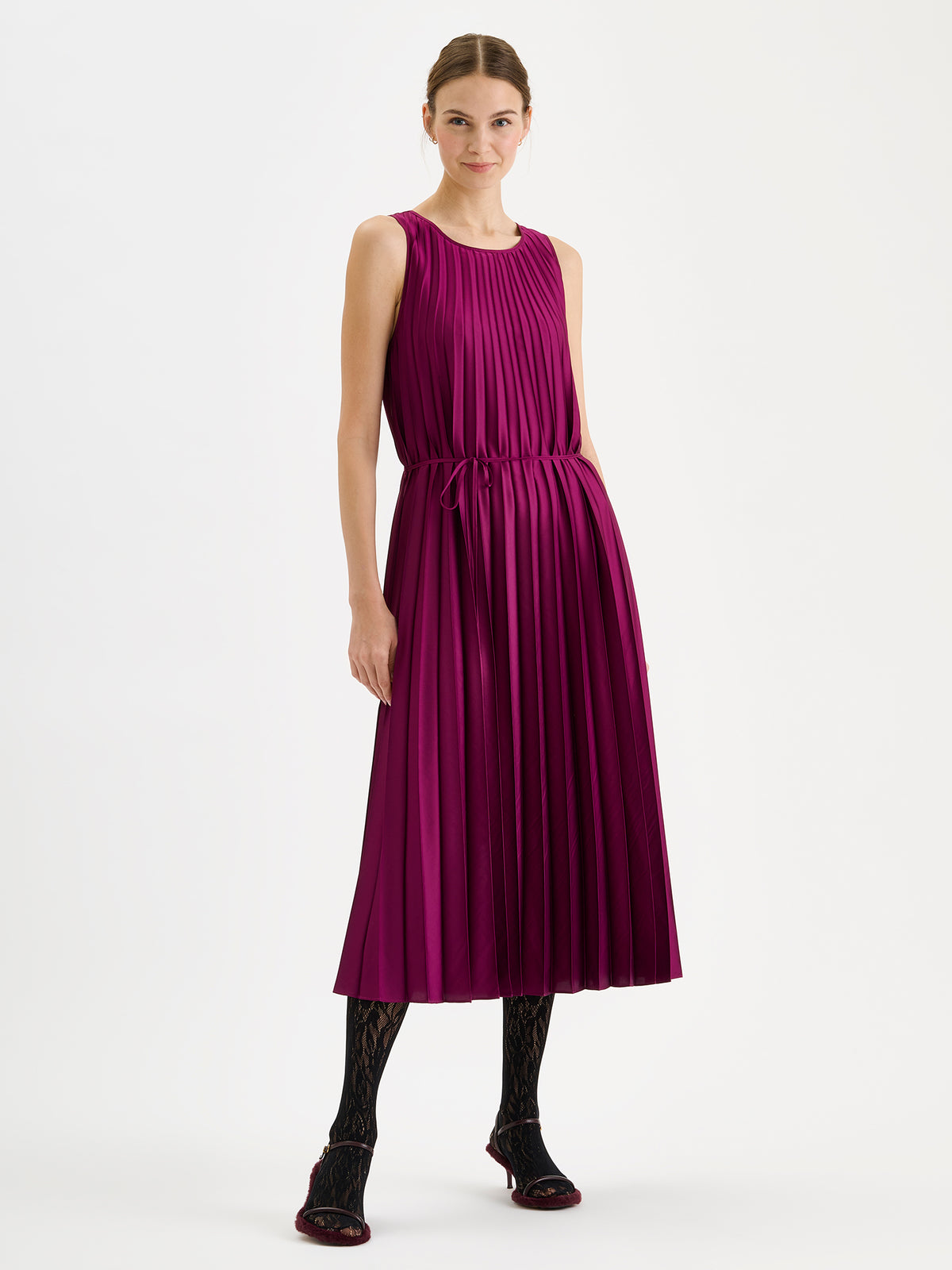 Nanso women's beautifully draping long Taite dress in a radiant violet shade. This long, sleeveless pleated dress with a slim belt is a striking choice for festive occasions and other special moments throughout the season. Pictured on a model with heels. | 36 - 180cm