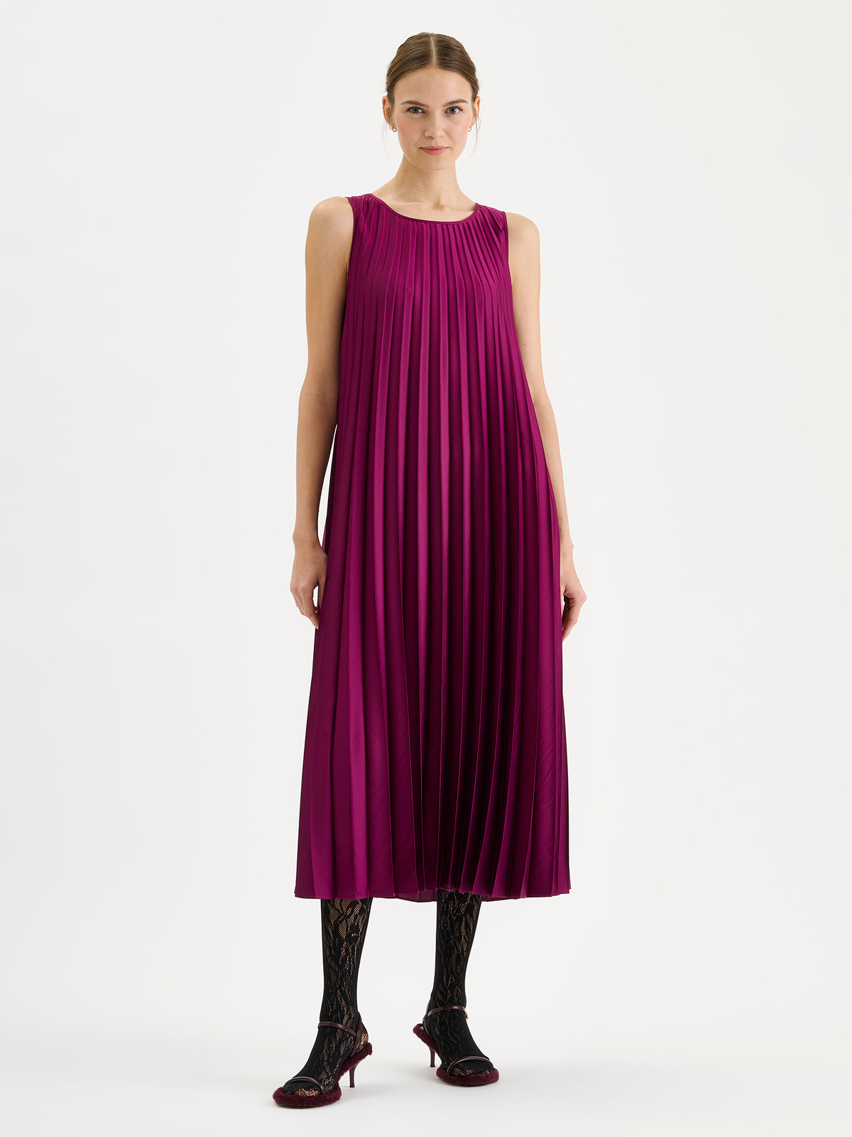 Nanso women's beautifully draping long Taite dress in a radiant violet shade. This long, sleeveless pleated dress with a slim belt is a striking choice for festive occasions and other special moments throughout the season. Pictured on a model with heels without the belt.