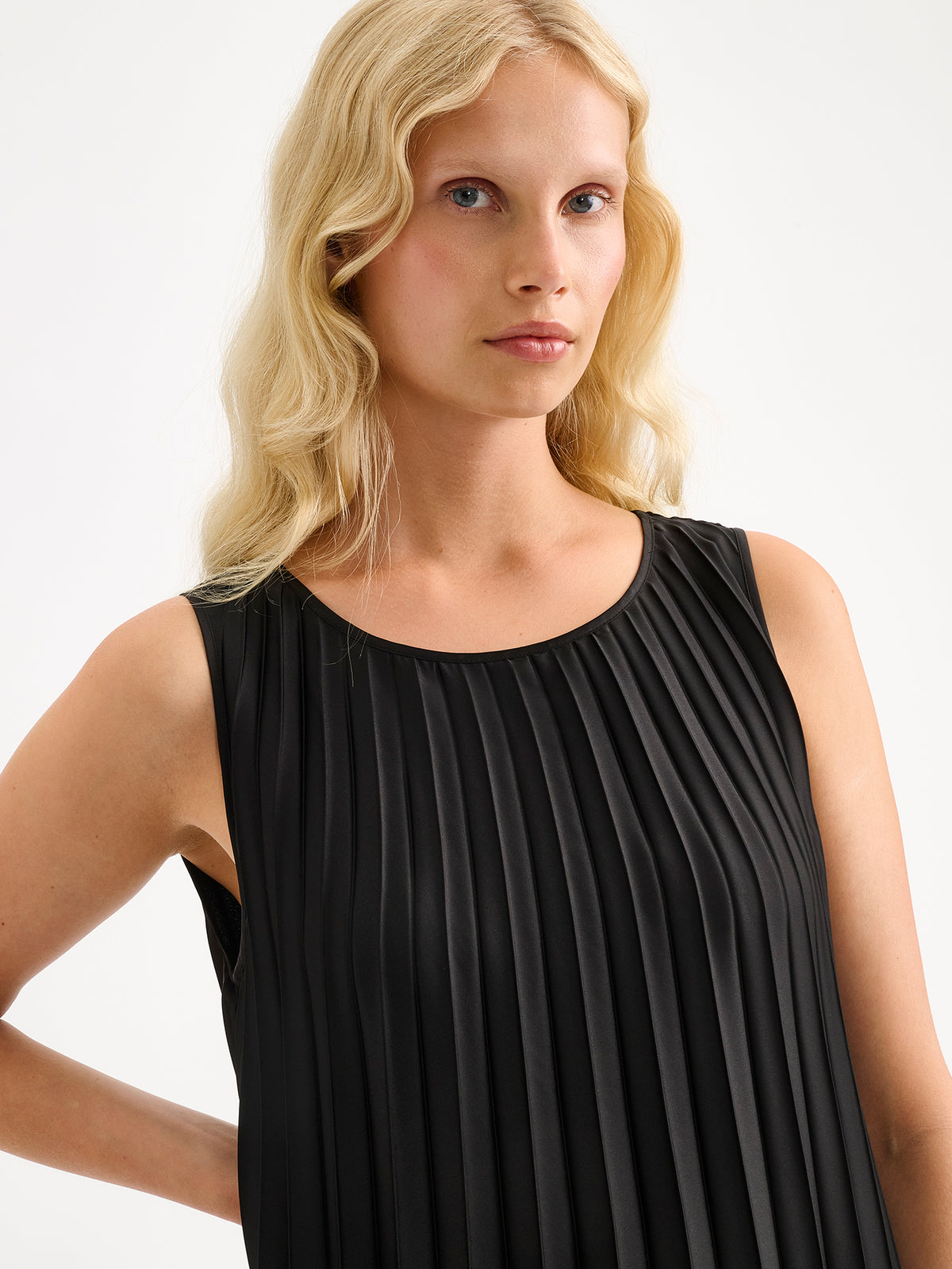 Nanso women's beautifully draping long Taite dress in a classic black shade. This long, sleeveless pleated dress with a slim belt is a striking choice for festive occasions and other special moments throughout the season. Pictured on a model close-up.
