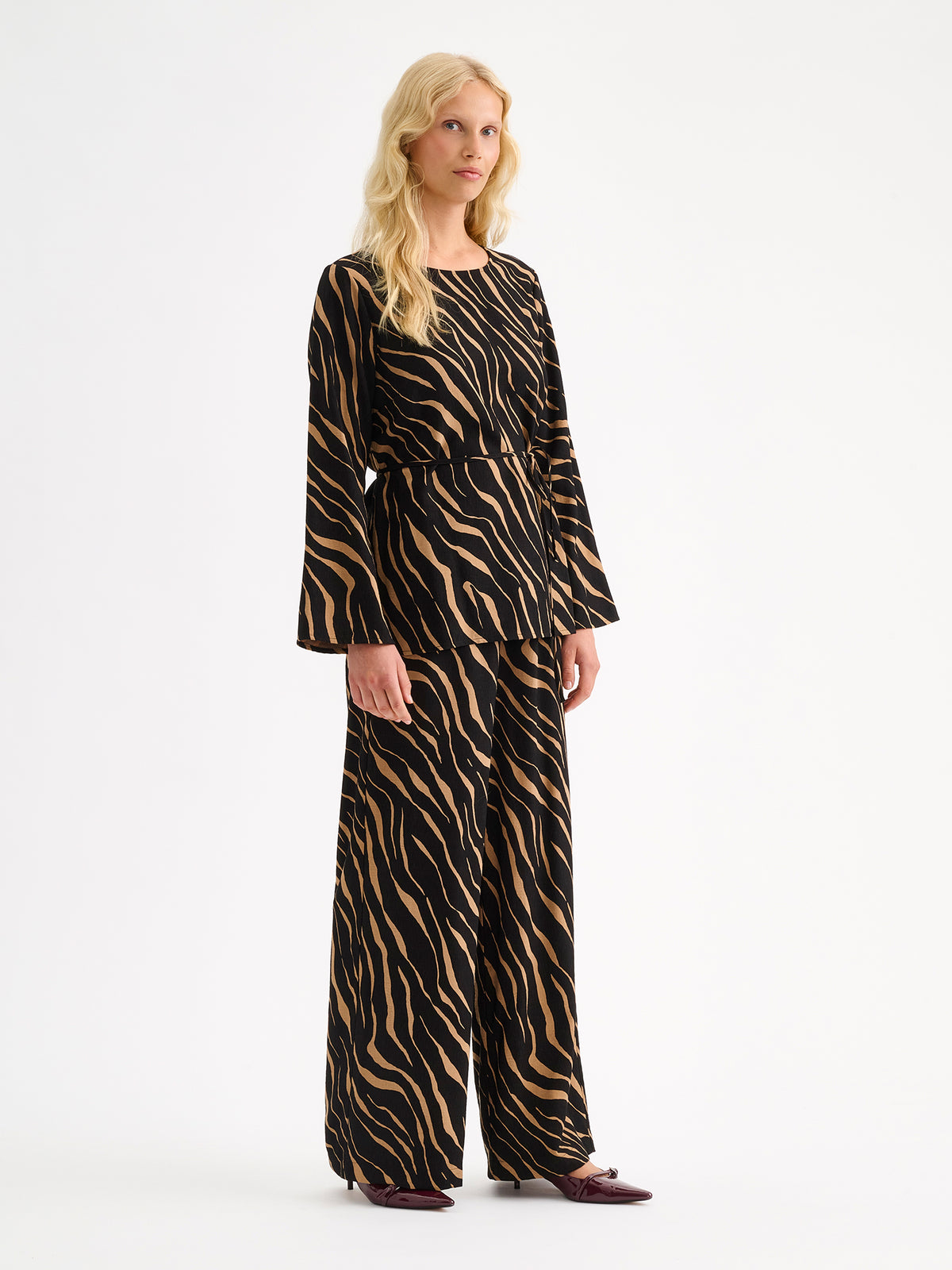 Nanso women's striking Sypressi belted blouse captivates with its elegant two-tone print, where shades of black and warm brown create a beautifully balanced look. Pictured on a blonde model with matching trousers.