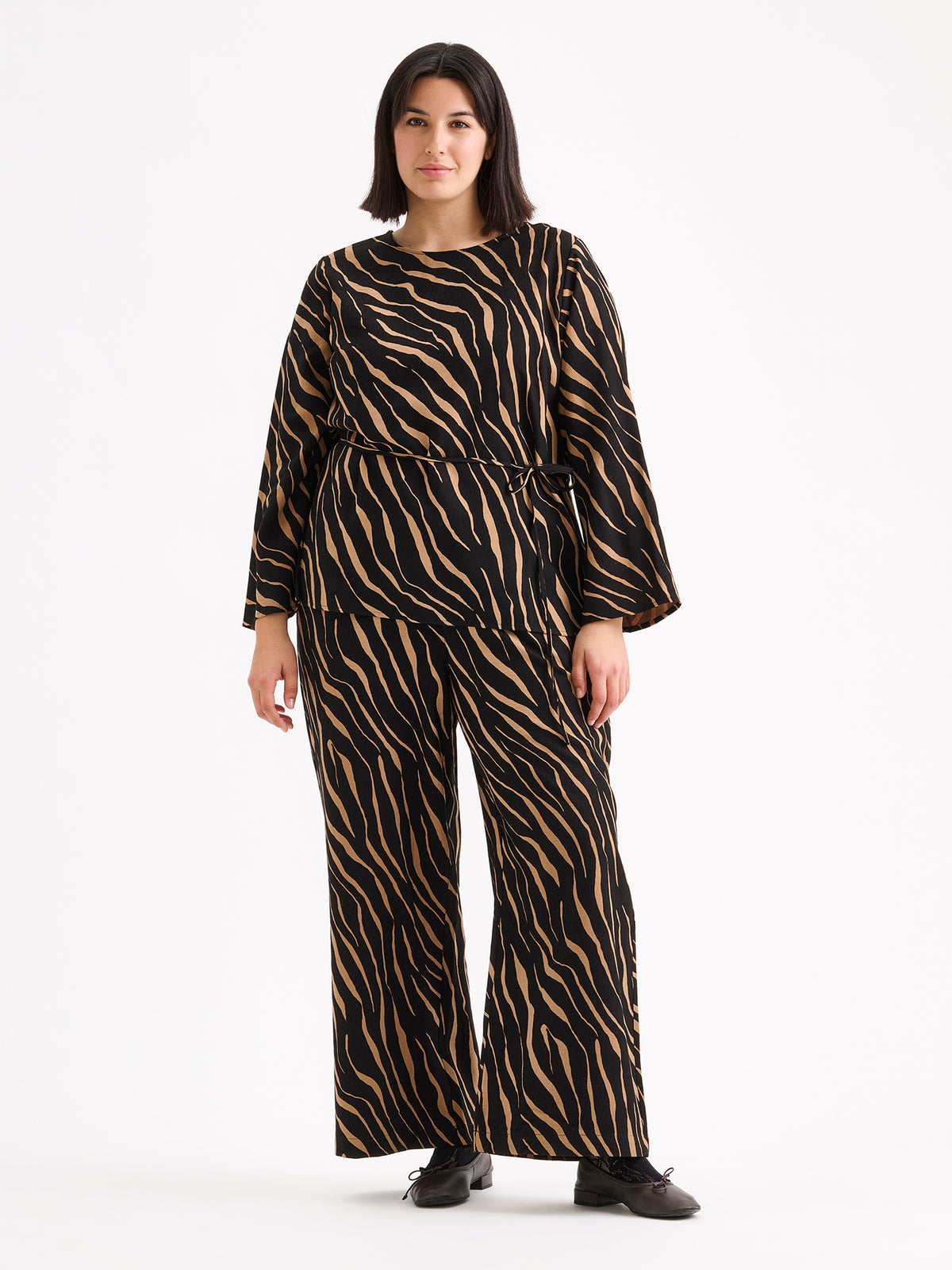 Nanso women's striking Sypressi belted blouse captivates with its elegant two-tone print, where shades of black and warm brown create a beautifully balanced look. Pictured on a brunette model with matching trousers.