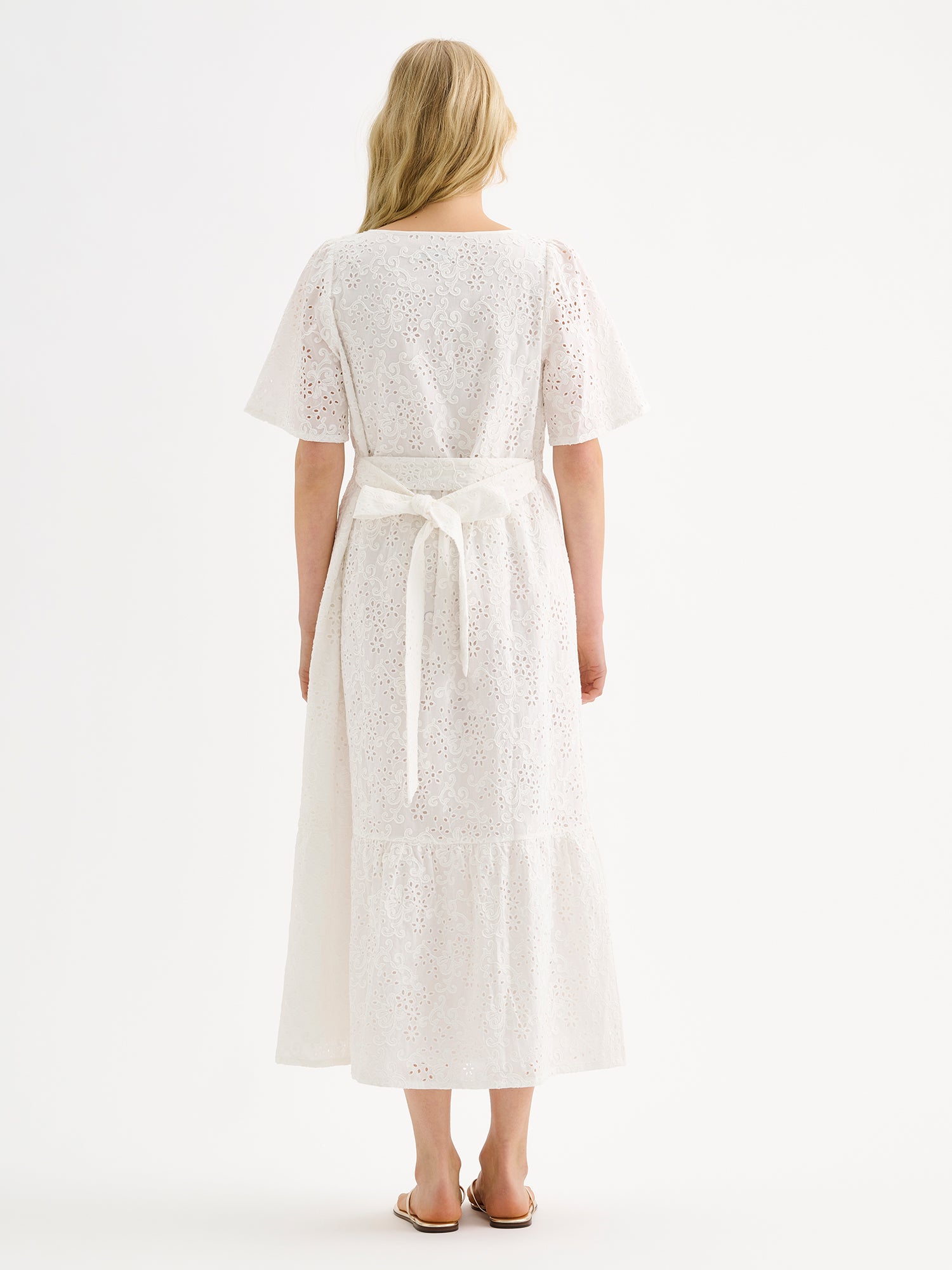 Nanso women's beautiful long soft white Odette dress crafted from delicate broderie anglaise style cotton fabric with a lace-like texture on a model with sandals, pictured from the backside.