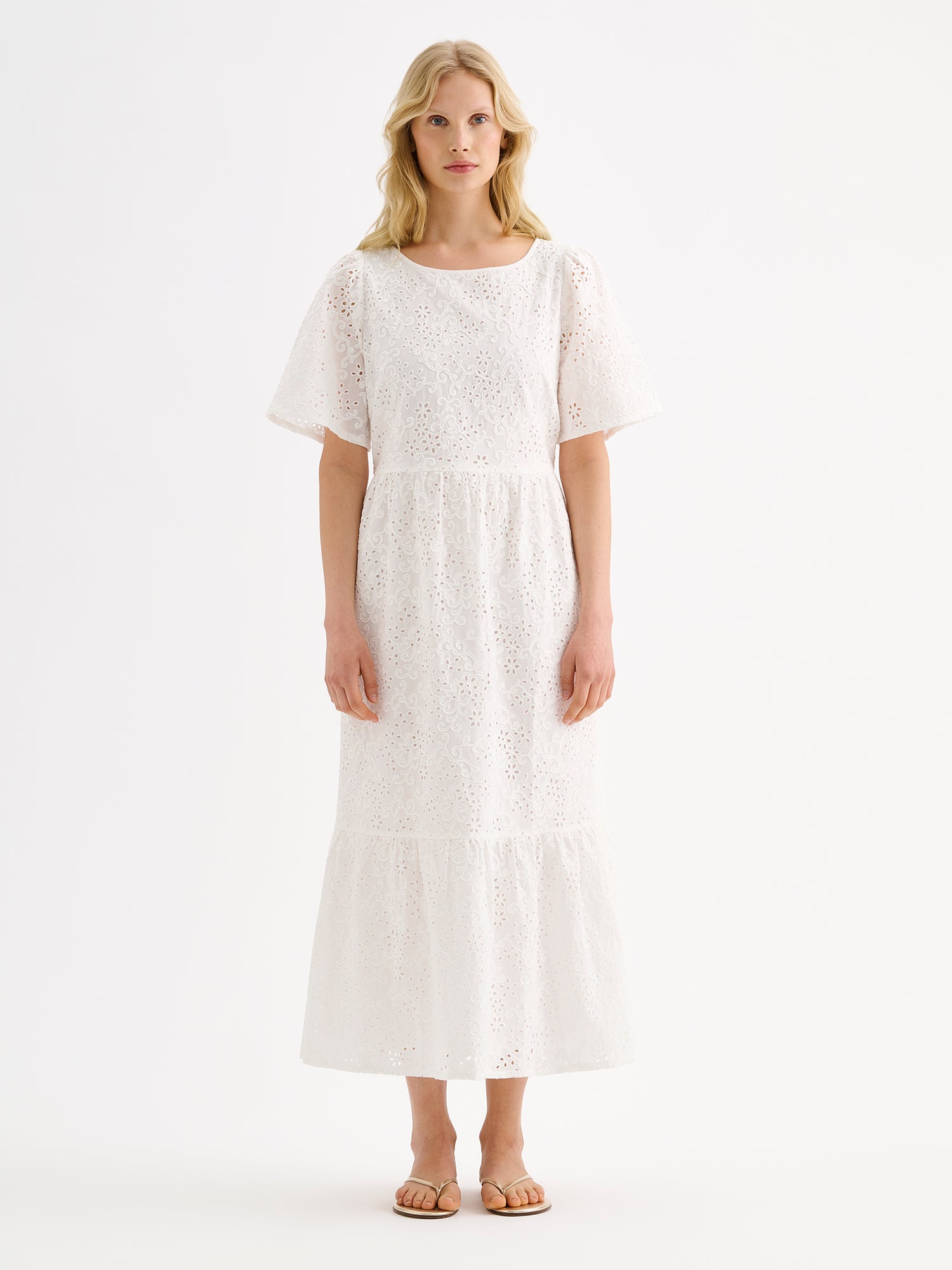 Nanso women's beautiful long soft white Odette dress crafted from delicate broderie anglaise style cotton fabric with a lace-like texture on a model with sandals.