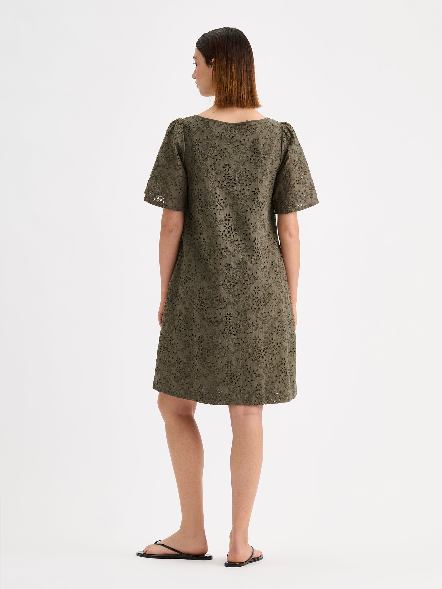 Nanso women's Odette Short Embroidered Dress in olive green, crafted from delicate broderie anglaise style cotton fabric, on a model pictured from the back side.