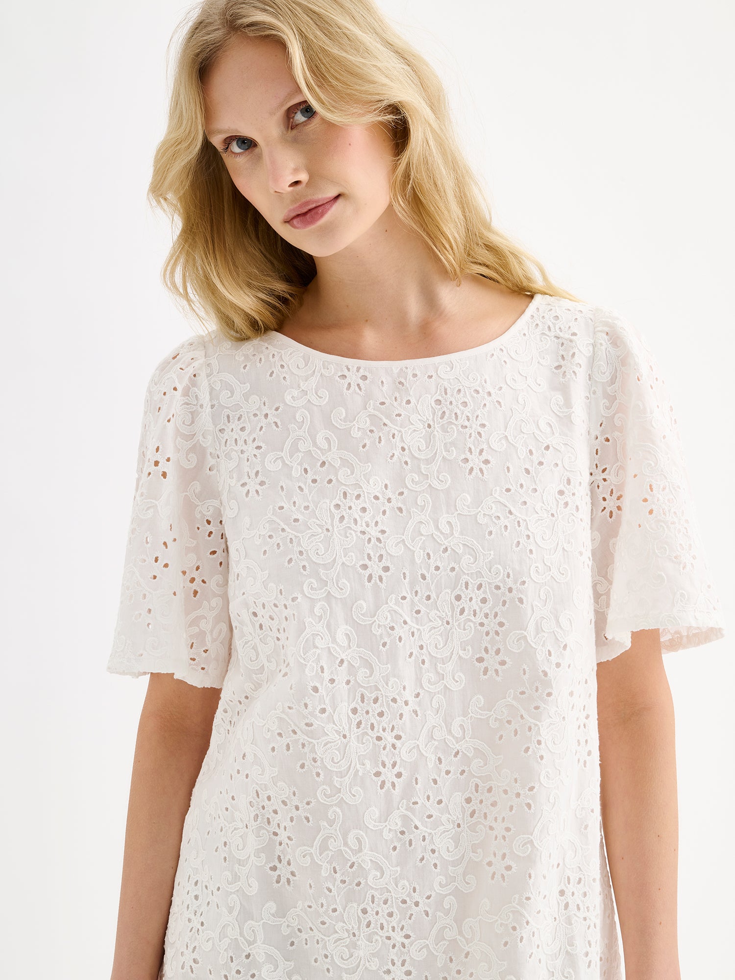 Nanso women's Odette Short Embroidered Dress in soft white, crafted from delicate broderie anglaise style cotton fabric, on a model, close-up.