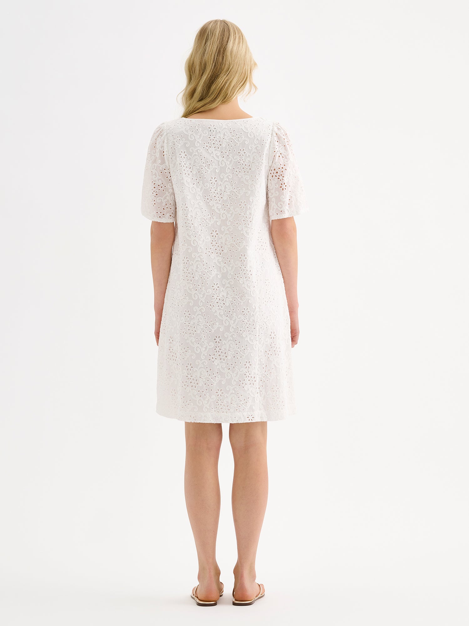 Nanso women's Odette Short Embroidered Dress in soft white, crafted from delicate broderie anglaise style cotton fabric, on a model with sandals, pictured from the back side.
