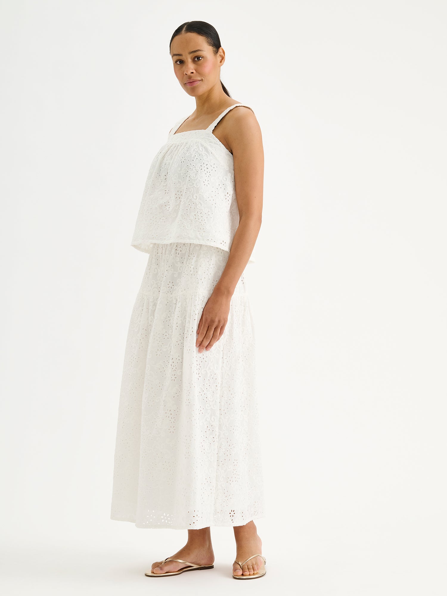 Nanso women's Odette skirt is a beautiful maxi-length skirt with a flowing silhouette, crafted from soft white cotton fabric featuring delicate broderie anglaise detailing, on a model with a matching top.