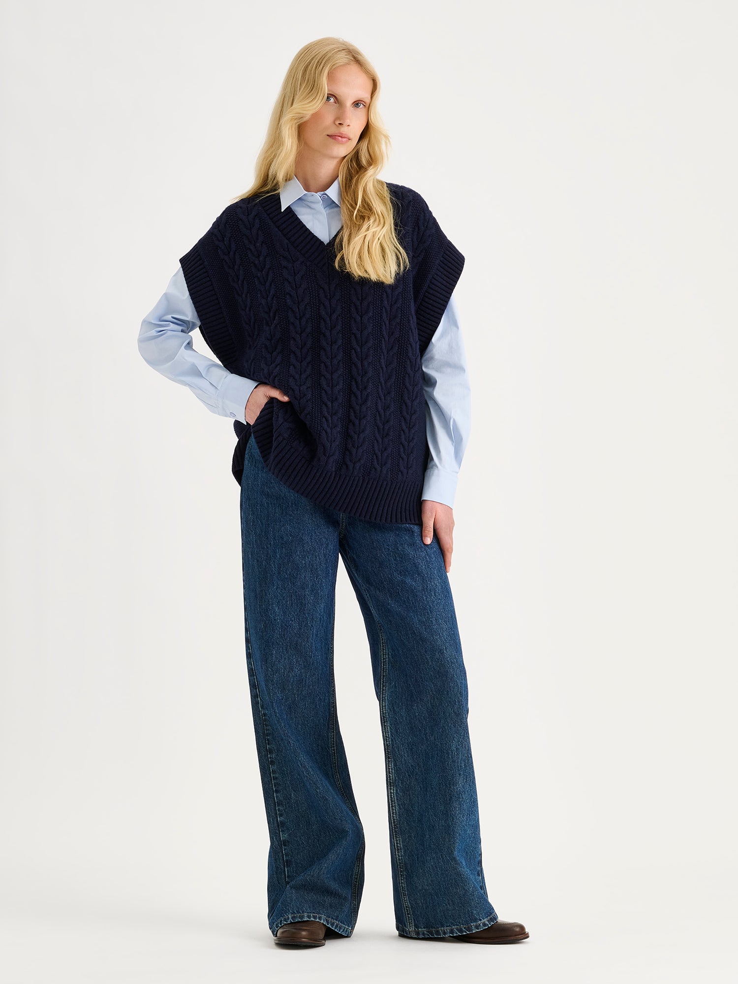 Nanso women's relaxed and generously cut Palmikot -knit vest on a blonde model with collared button up shirt and blue jeans