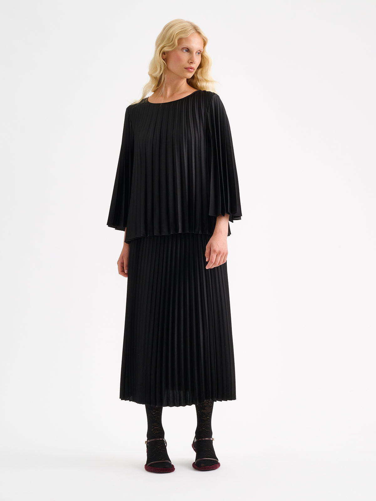 A model wearing a black outfit with a pleated skirt and blouse. | 36 - 175,5cm