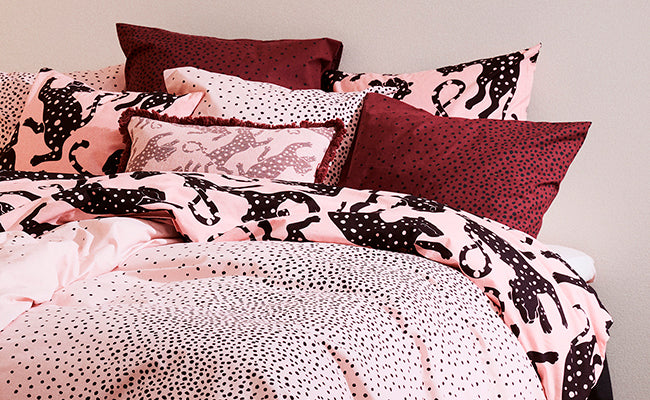 Bed with Täplä and Leonora bedding and pillows against a neutral wall