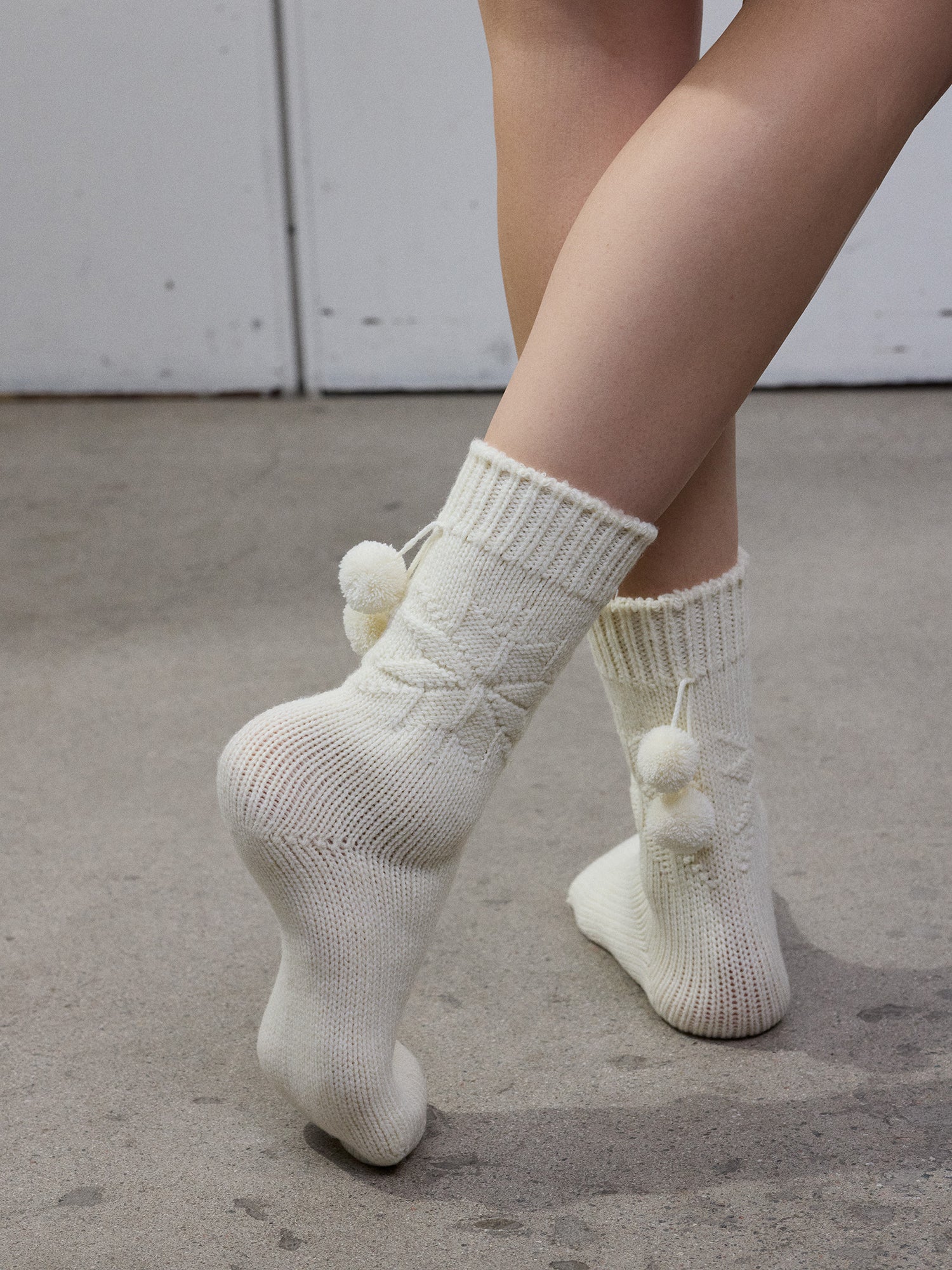 The off-white Miriam wool blend socks with snowflake pattern and pompoms worn by a model.