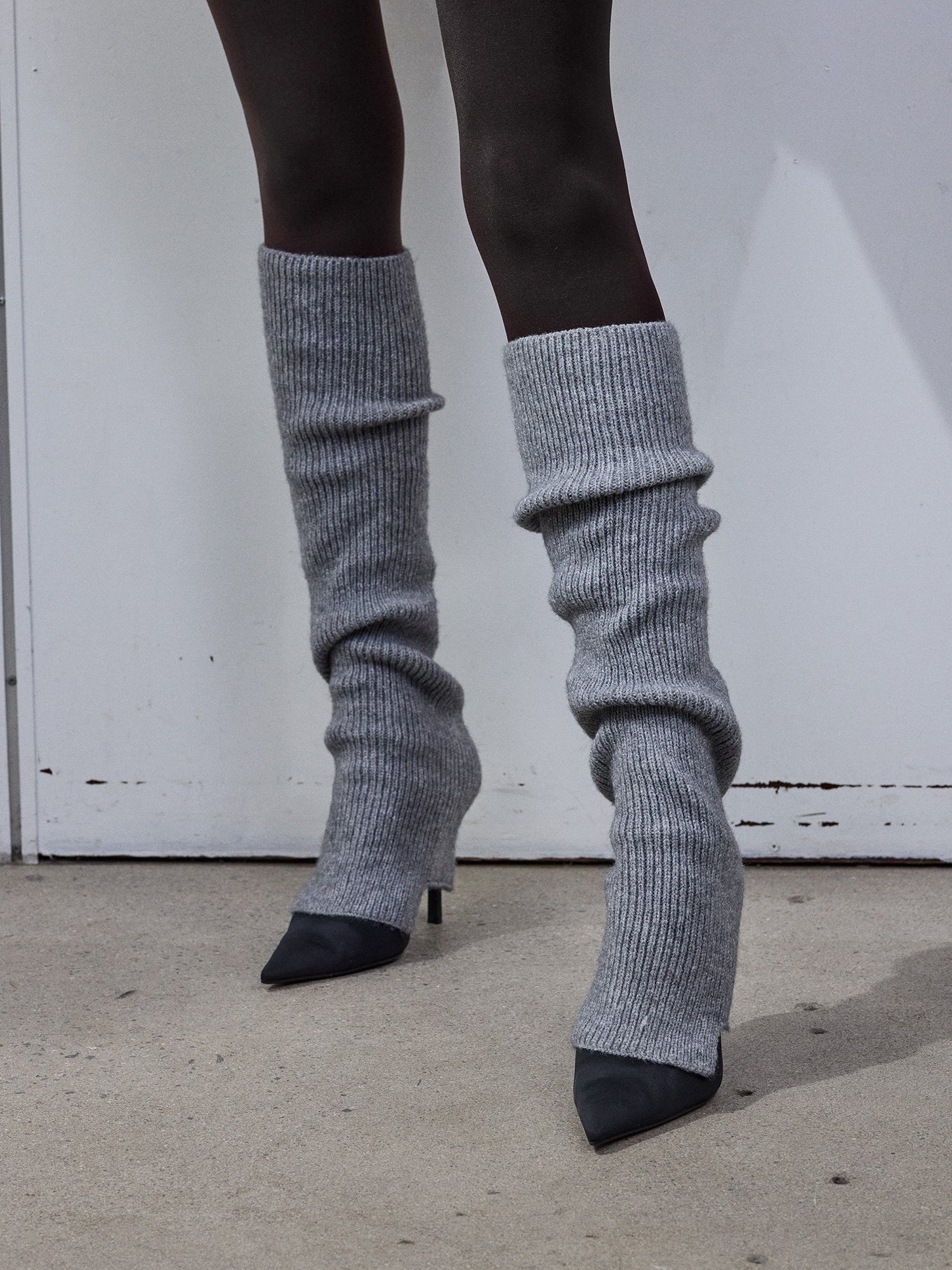 The Merina leg warmers in melange grey with black heels and black tights on a model in the picture.