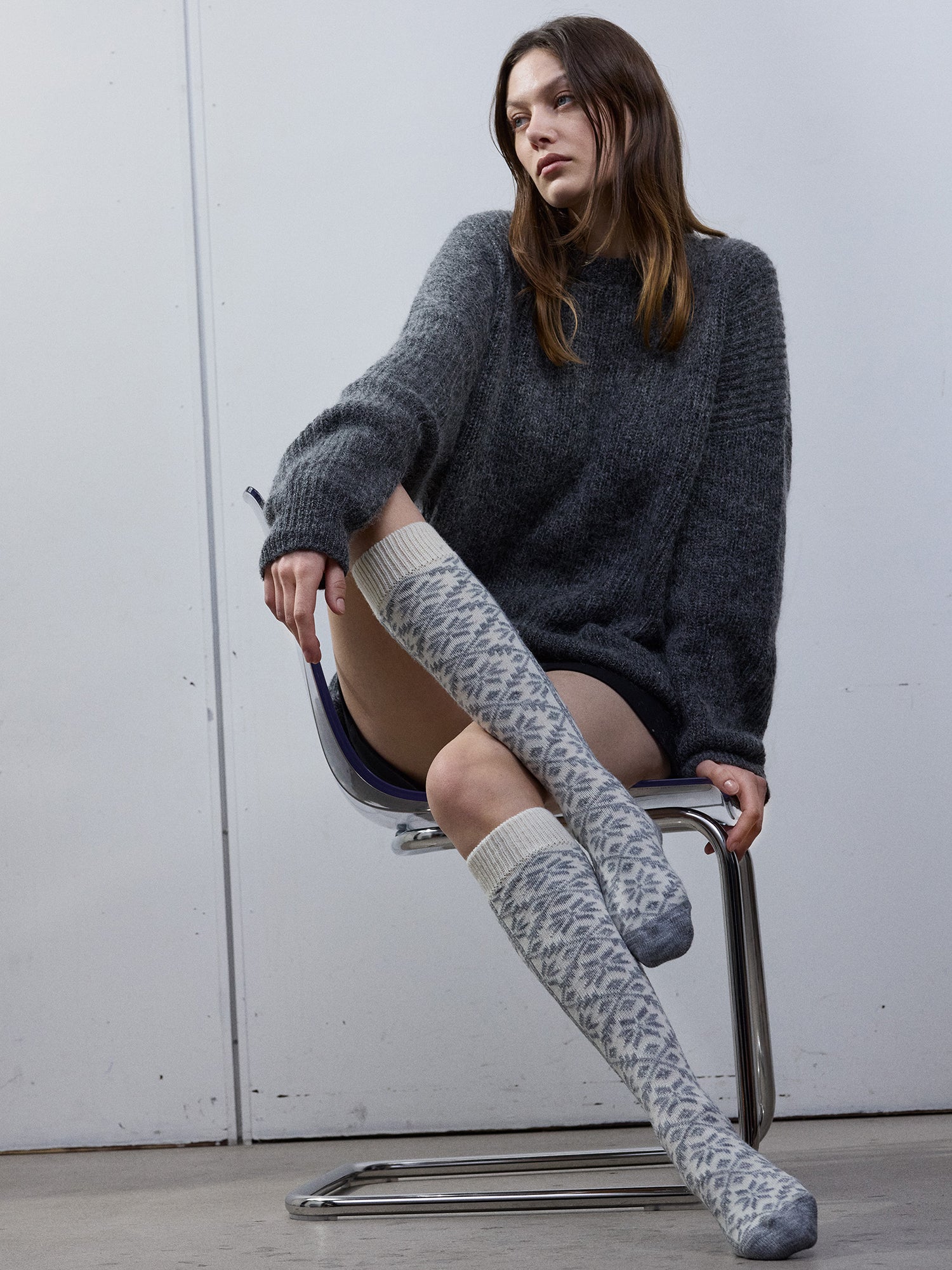 Model wearing a gray sweater and patterned off-white knee-high socks sitting on a chair in the photo.