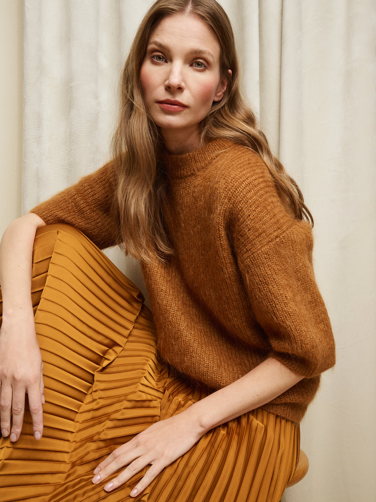 Nanso women's wonderfully warm and luxurious Sumi knitted sweater in rich brown and beautifully fluffy texture, on a model with a pleated brown skirt.