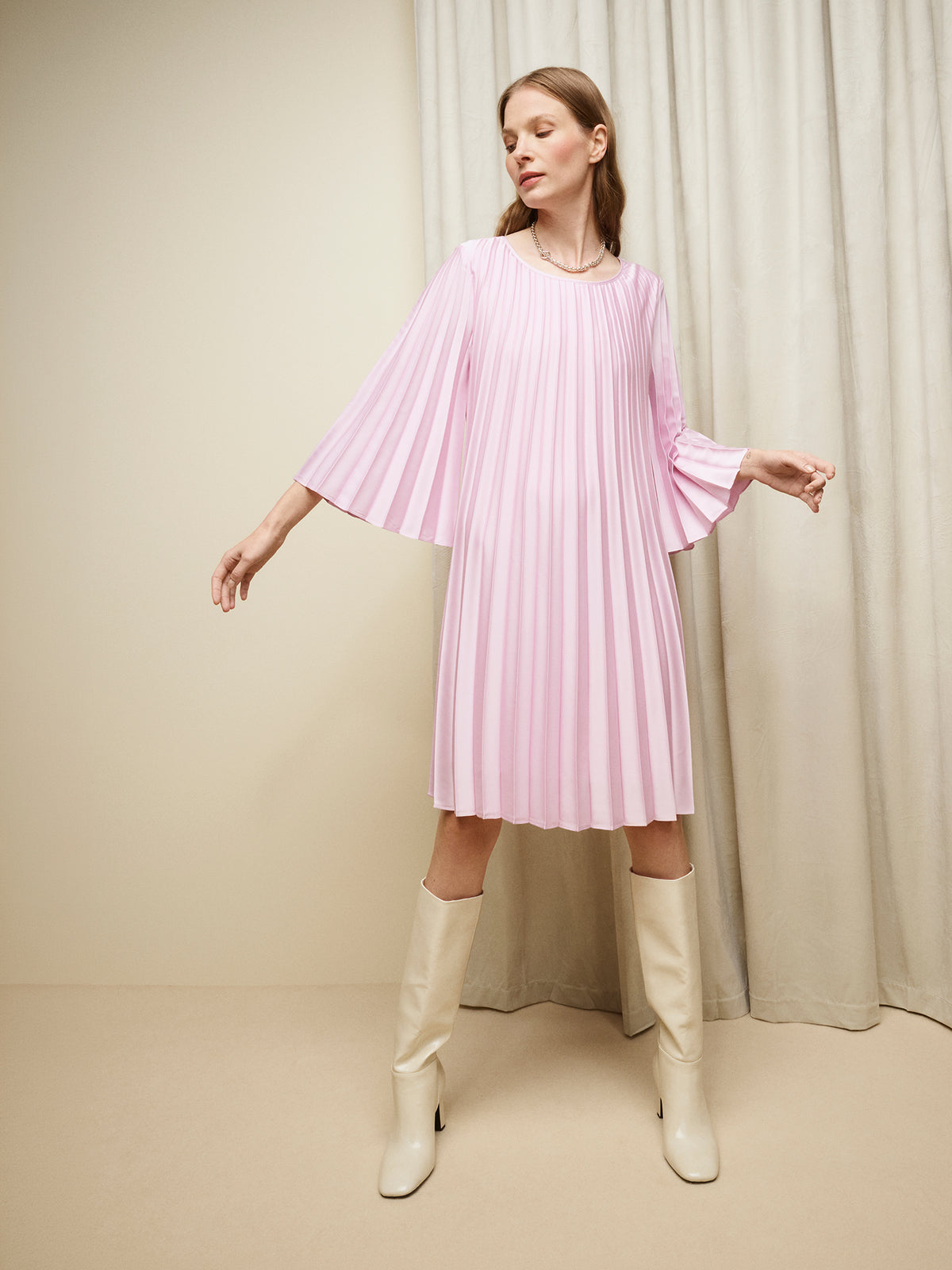Nanso women's beautifully draping Taite dress in a deliciously cool light pink shade. This versatile pleated dress can be worn with or without the slim belt. This A-line dress features 3/4-length sleeves and a slim belt at the waist. Pictured on a model with off white boots. | 36 - 175,5cm