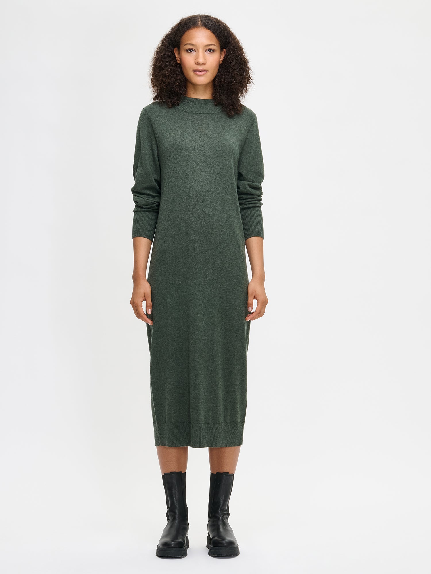 Nanso women’s dark olive green Villis knit dress in a merino wool and cotton blend, stand collar, full-length sleeves and calf-length hem, worn by model in full-body view.