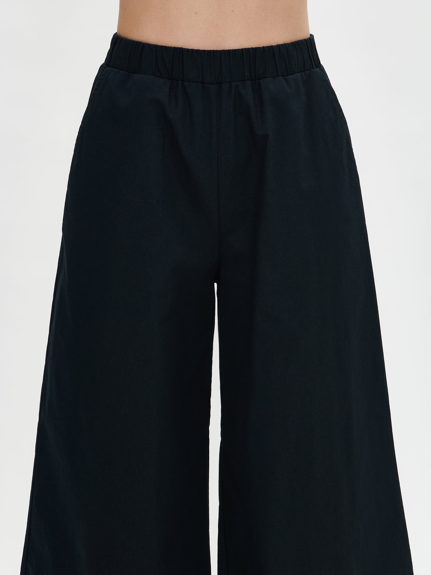 Nanso women's relaxed black Hyppy trousers from the front in a close-up. 7/8-length wide legs, elastic waistband and side pockets. Easy to style with various tops. In a close-up image on the model.
