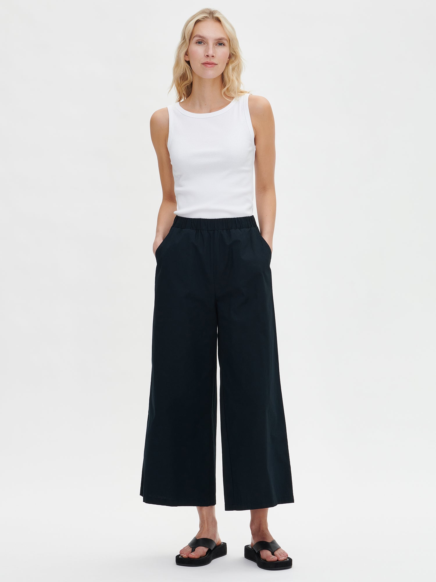 Nanso women's relaxed black Hyppy trousers from the front. Wide-leg 7/8-length trousers with an elastic waistband and side pockets. Made of structured cotton poplin. In a front-facing product image.