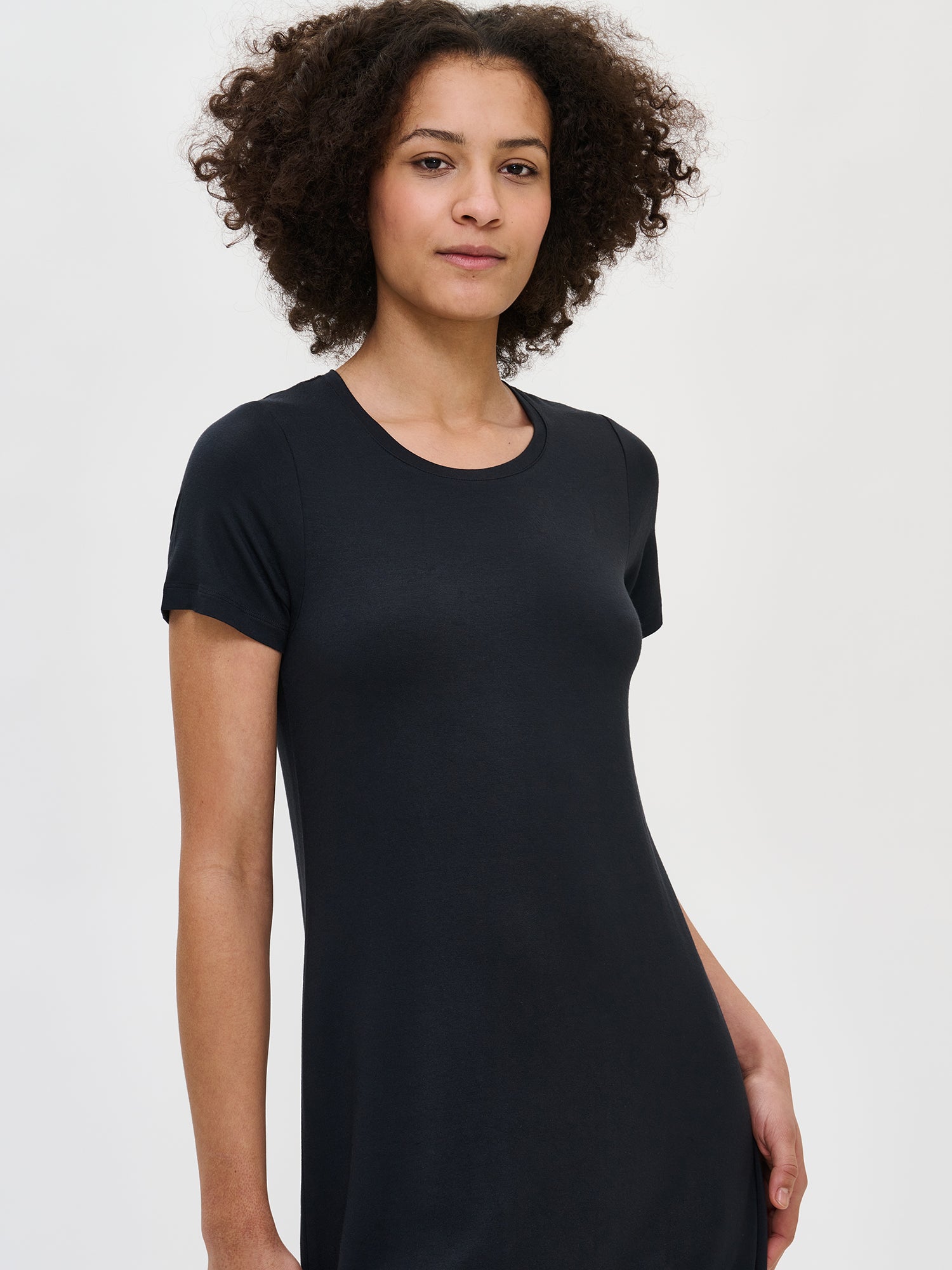 Nanso women's luxuriously soft black Pitsi nightgown with short sleeves, a round neckline, and a timeless lace-trimmed hem, worn by the model in a close-up front view.