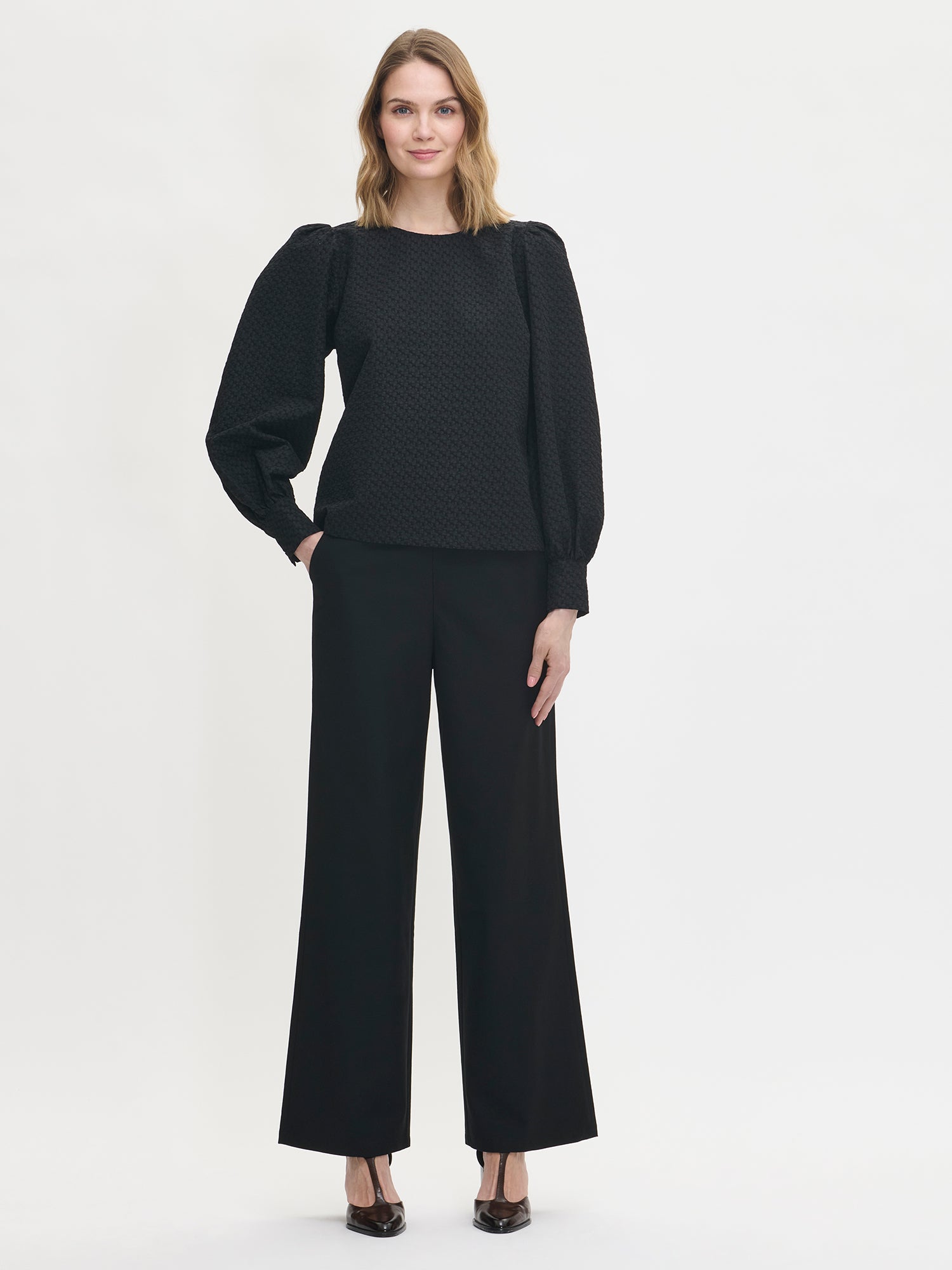 Nanso's stylish women's blouse in black features a beautiful textured surface. From the front styled with black pants.