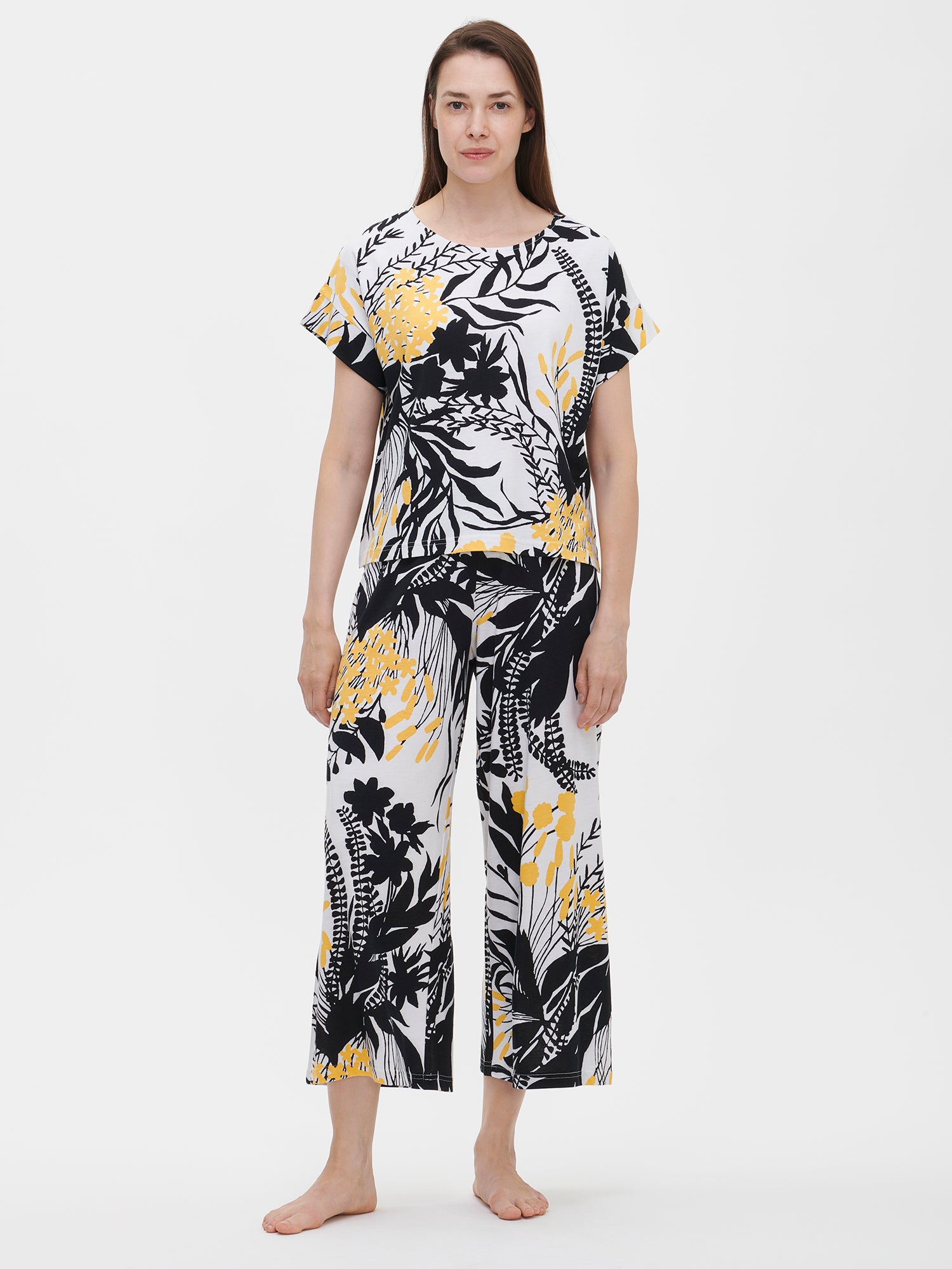 Nanso women’s floral-patterned pants with black and yellow flowers and leaves on a white background. These high-waisted, wide-leg 7/8-length Puutarha lounge pants, worn by the model.
