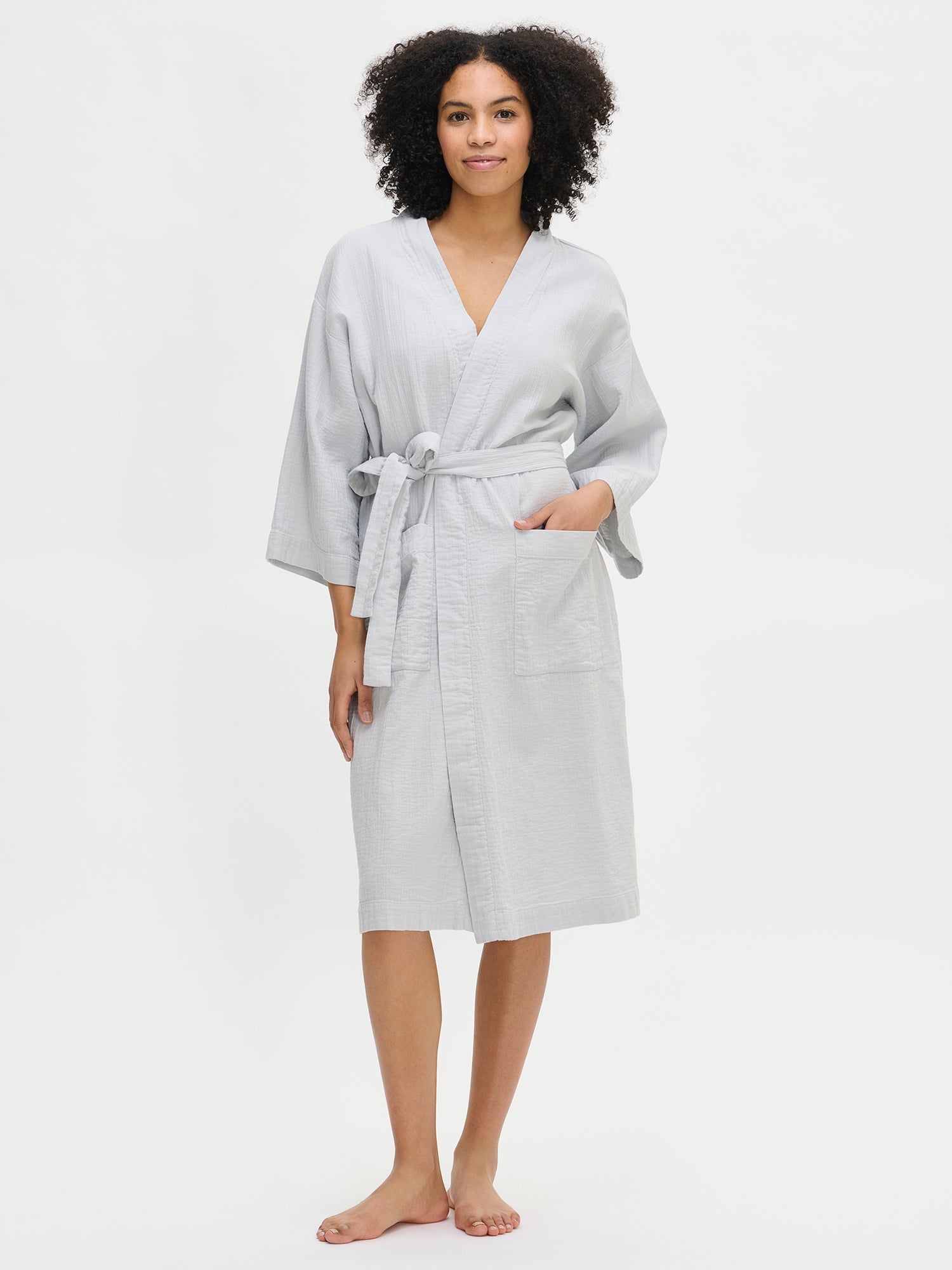 Nanso women's comfortable solid blue Aamu bathrobe with a knee-length hem, featuring kimono-style sleeves, a neckline finished with a wide trim, patch pockets, and a belt attached with belt loops, worn by the model.